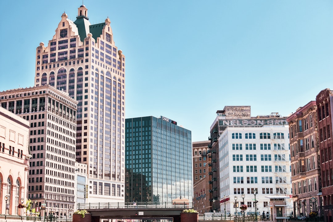 Historic ornate tower and glass office building rise above a downtown street under blue sky.