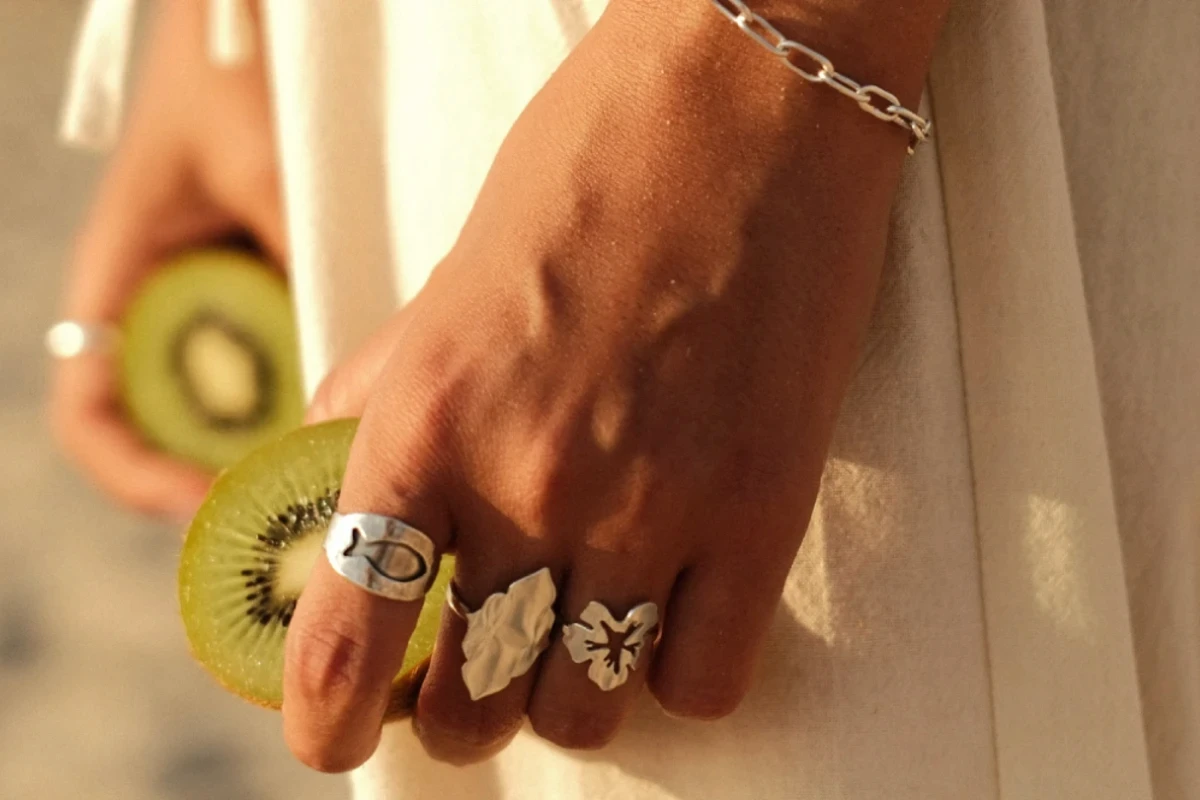 צילום לייף-סטייל אסתטי של יד אישה המעוטרת בטבעות כסף מעוצבות האוחזת בחצי פרי קיווי. התמונה משלבת טקסטורות טבעיות ותאורת שמש רכה, מאת Shiriz Photography והצלמת שירי עציץ.