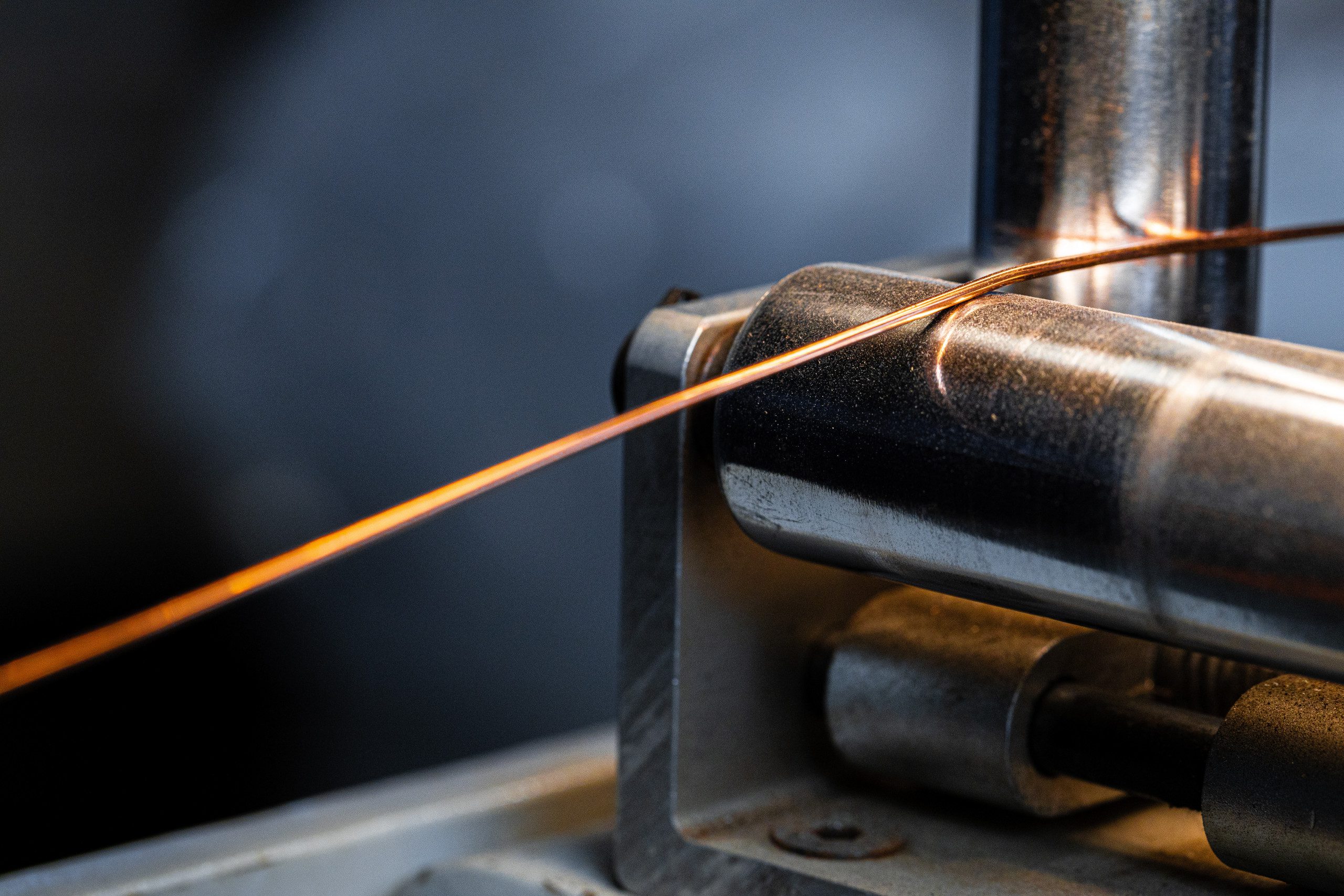 Close-up of a copper wire being processed by industrial machinery.