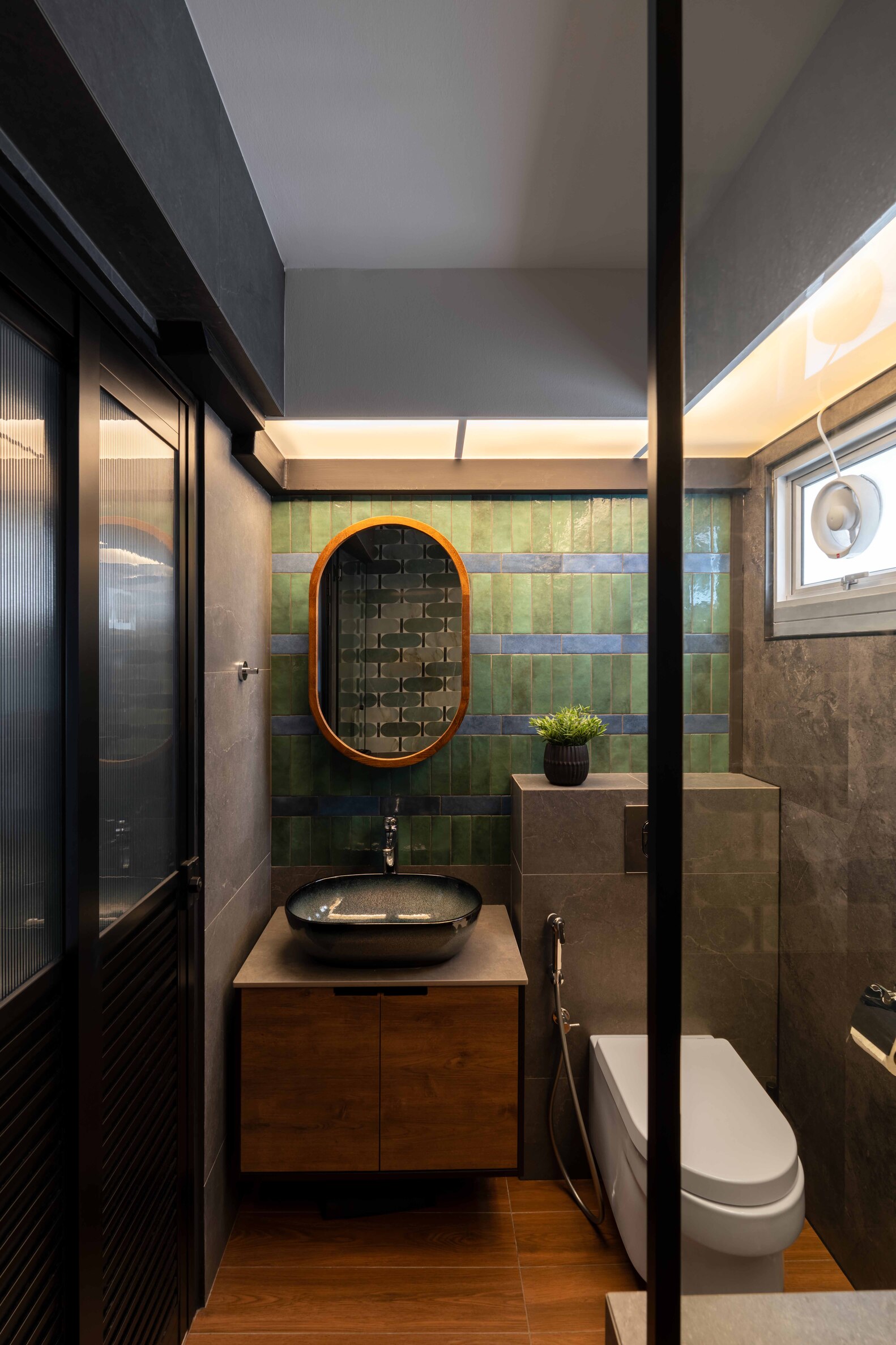 Modern bathroom featuring a dark color scheme, minimalist design, a wall plant, and stylish fixtures.