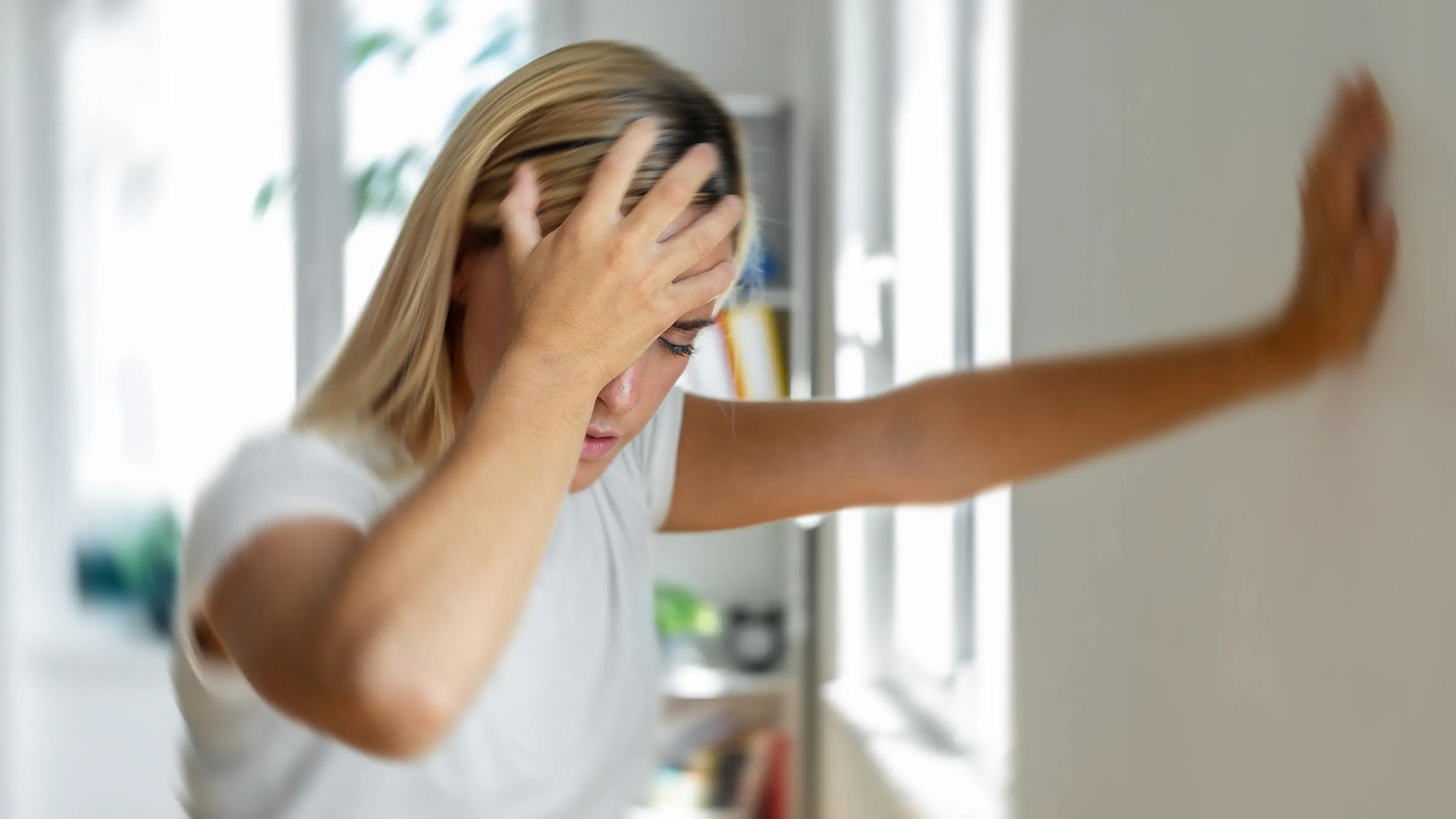 Woman dizzy with arm against wall, holding head