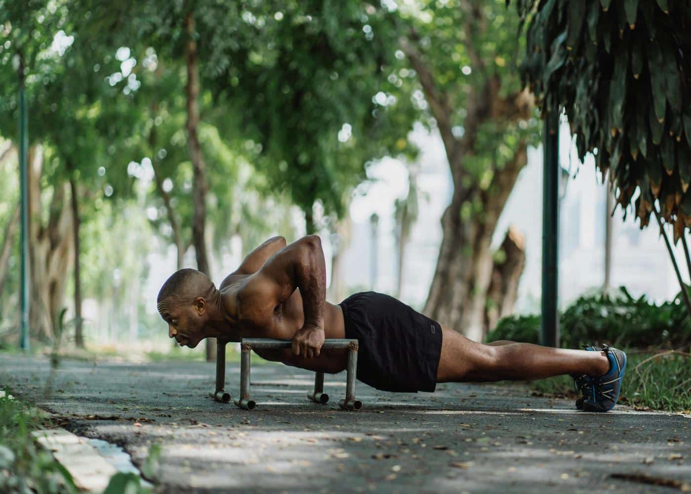Man without shirt doing pushups on low dip bars outdoors