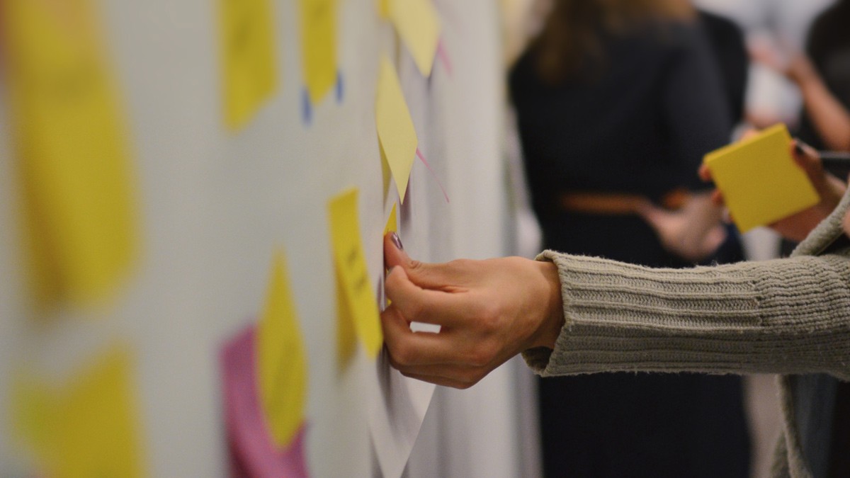 A workshop facilitator sicking a yellow sticky note on a whiteboard.