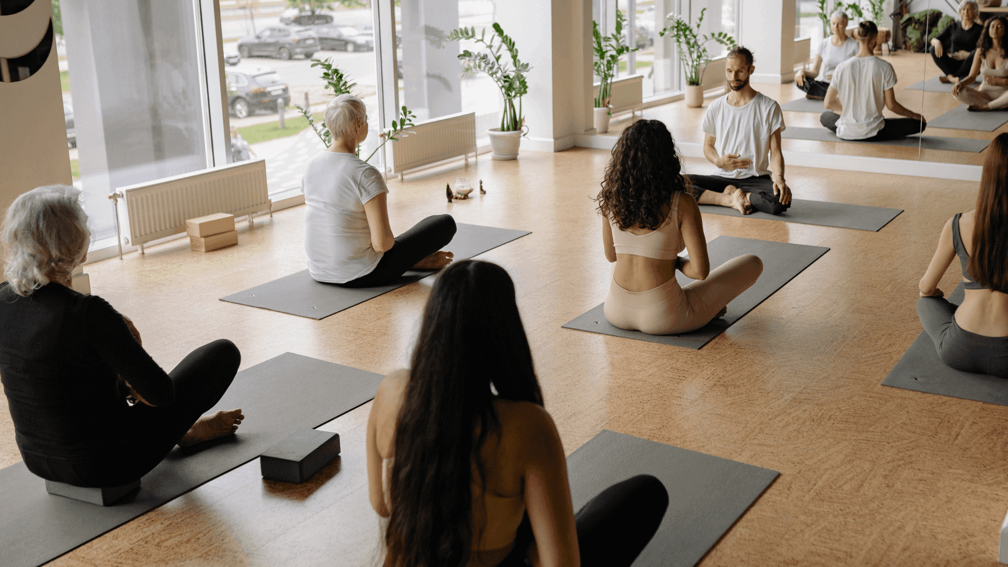 A new yoga teacher sitting at the front of his class with a group of mixed ability students.