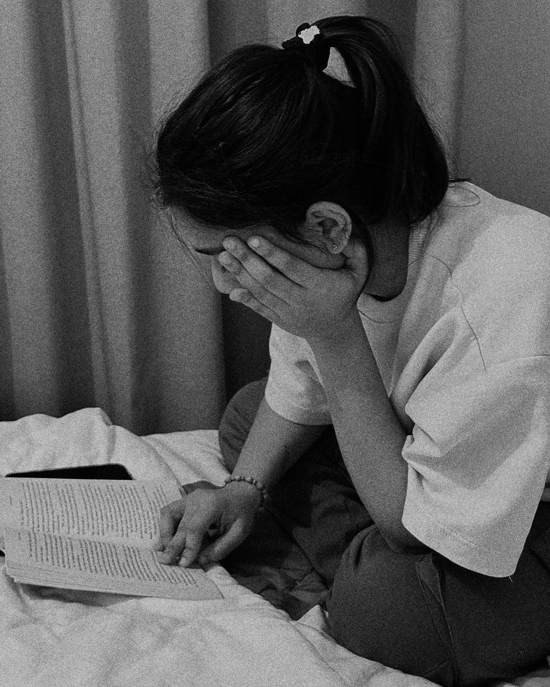 A thoughtful young person with dark hair gazes to the side, captured in soft black and white lighting.