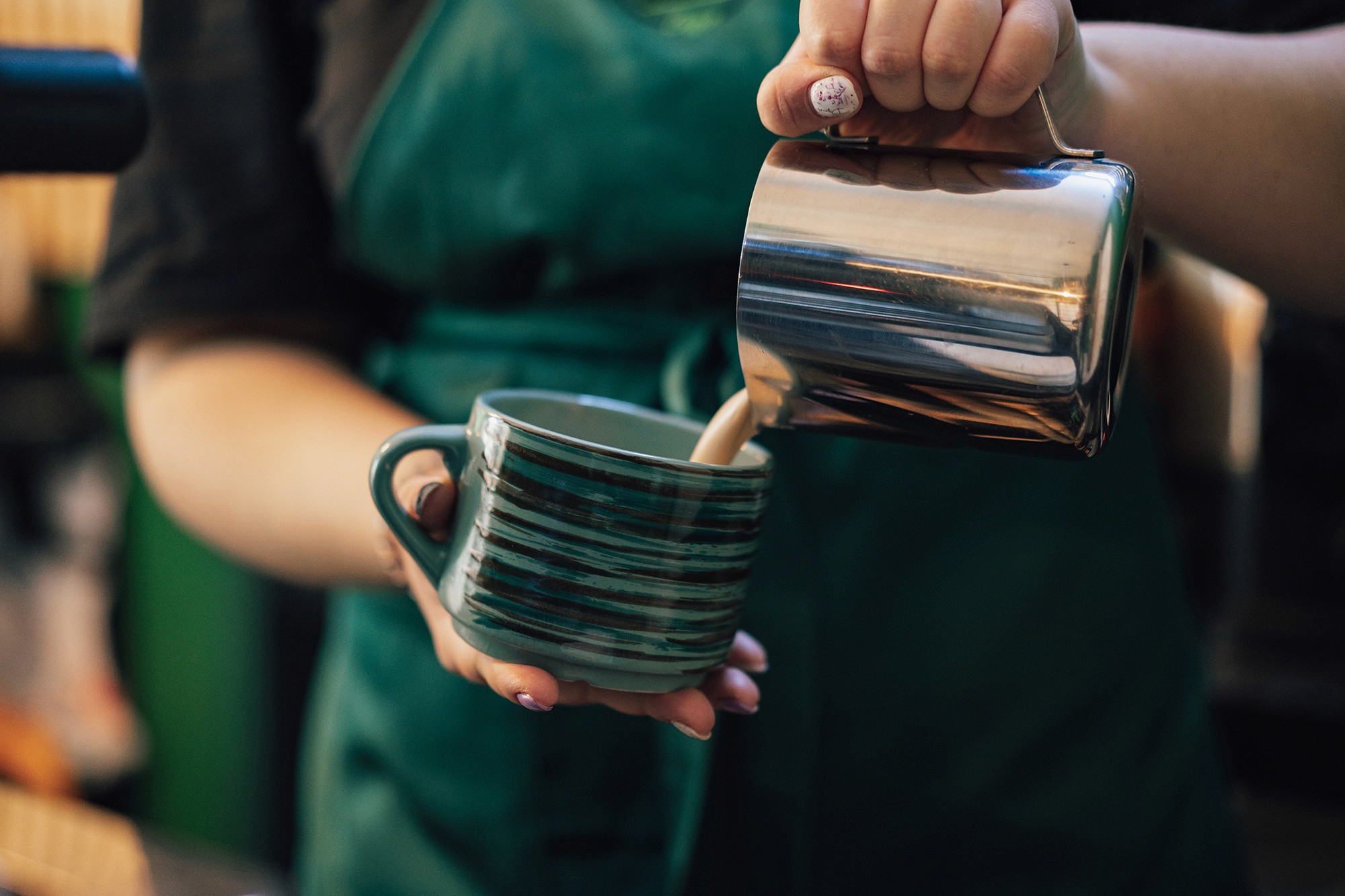 Barista pouring milk into striped ceramic mug