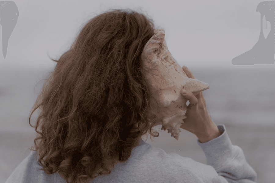 Woman holding a large seashell against her ear while facing the sea.