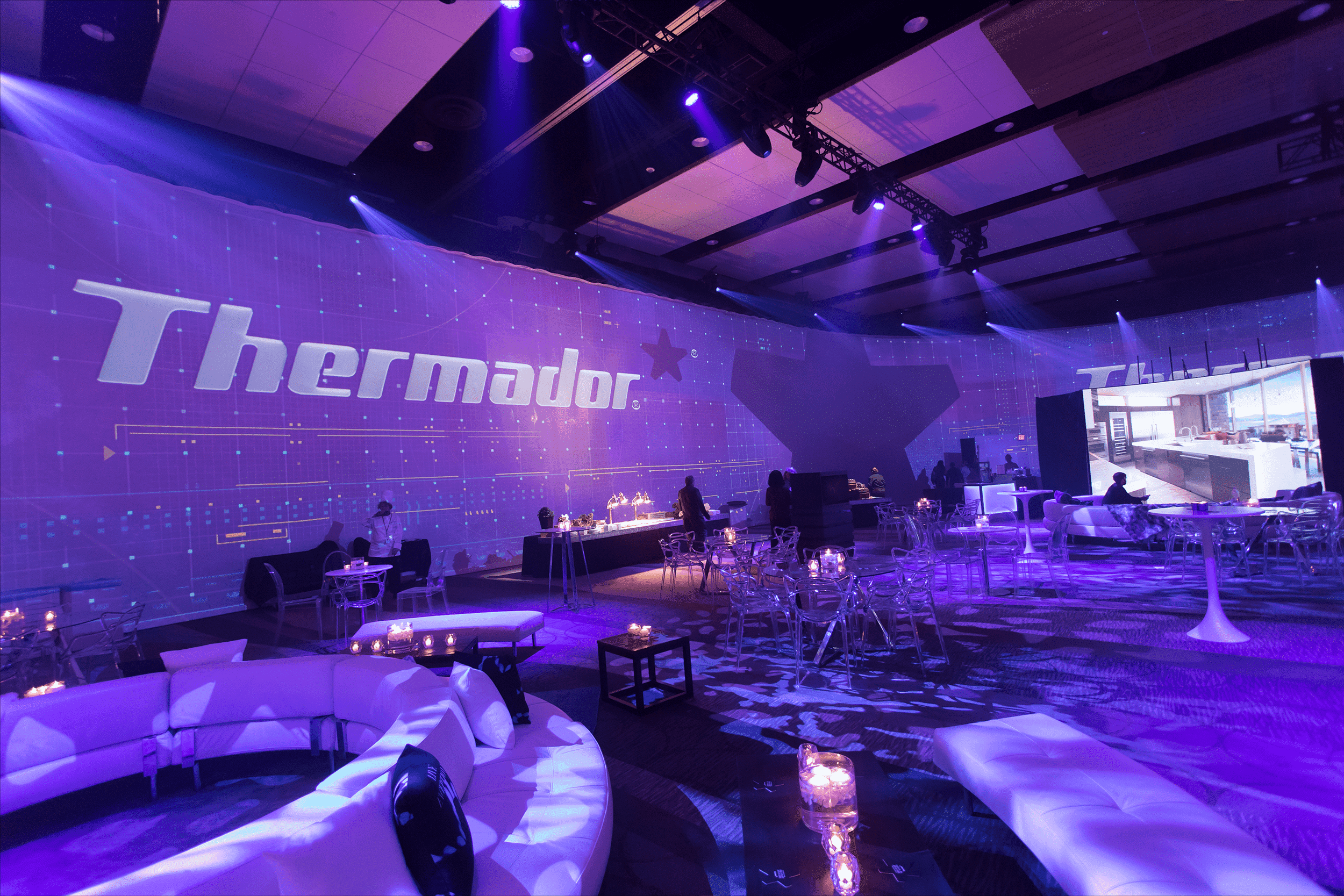 Thermador ballroom before attendee arrivals, logo on the wall with custom white seating in blue hue lighting