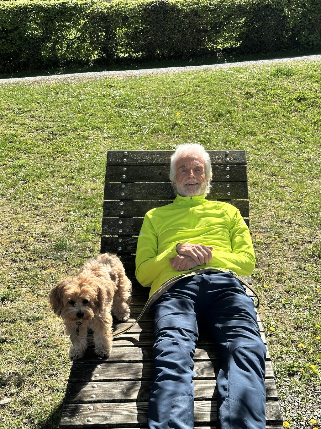 Johannes Nawroth Sitzend auf einer Holz liege in einer grünen Wiese, mit seindem Hund