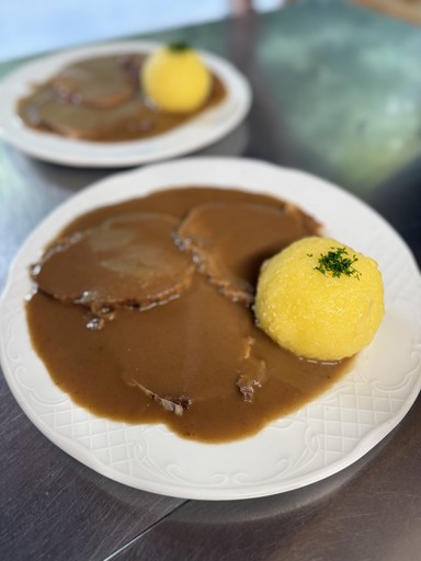 Smiling young woman with long hair standing against a dark green background, holding a finger to her chin.