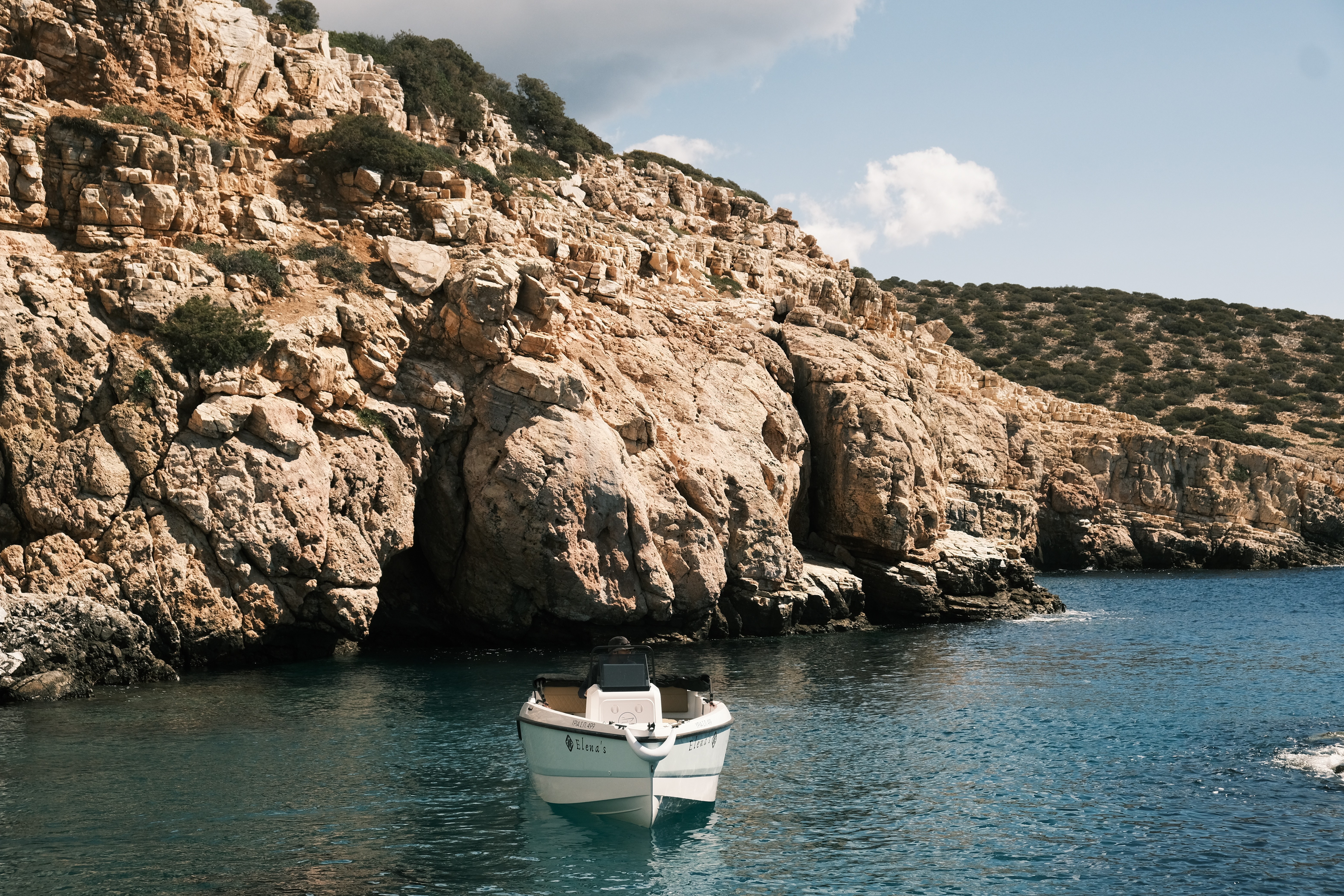 White Compass 16Oe yacht anchored in a secluded cove with dramatic limestone cliffs and crystal-clear turquoise waters in the Cyclades.