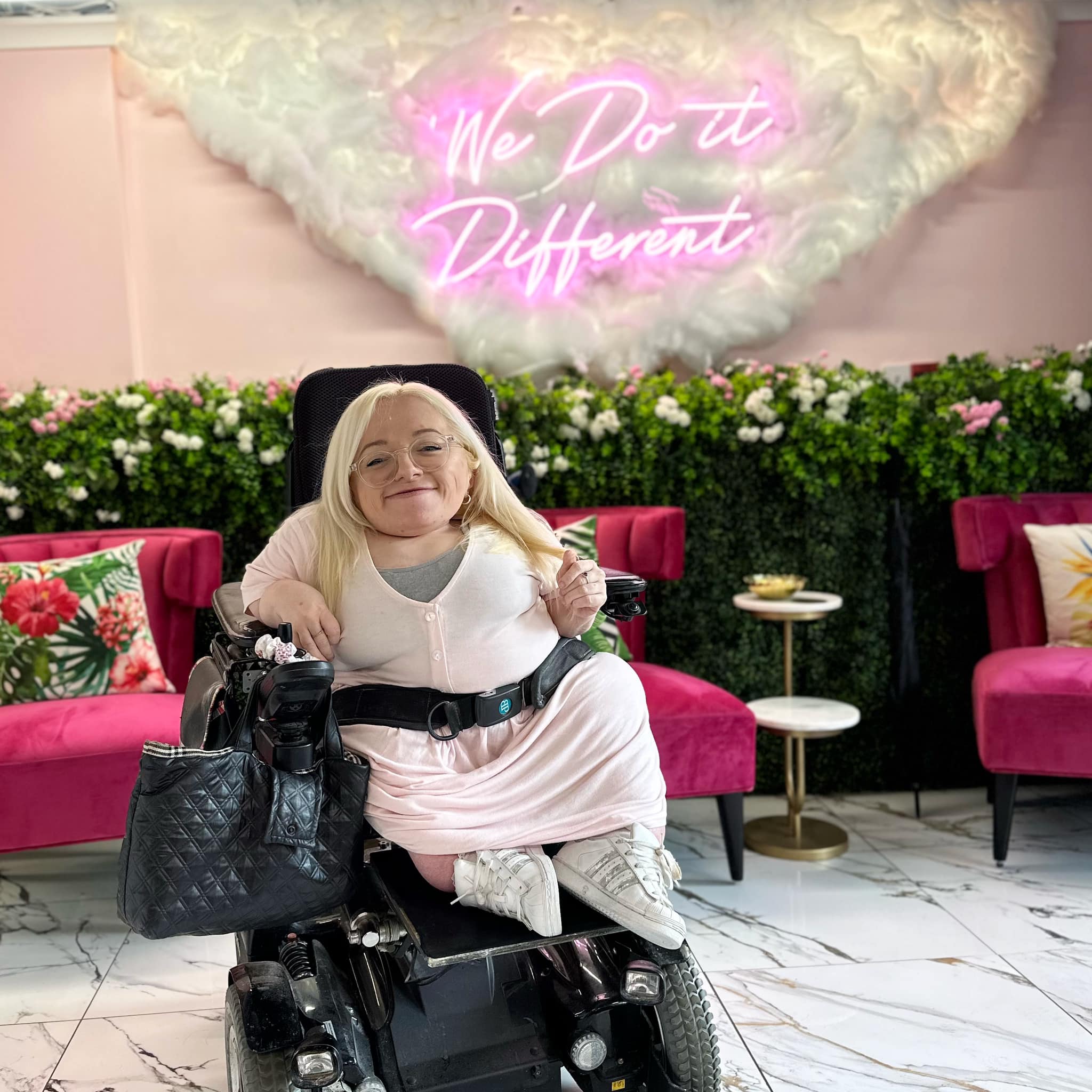 Gem in wheelchair in front of sign "We do it different"