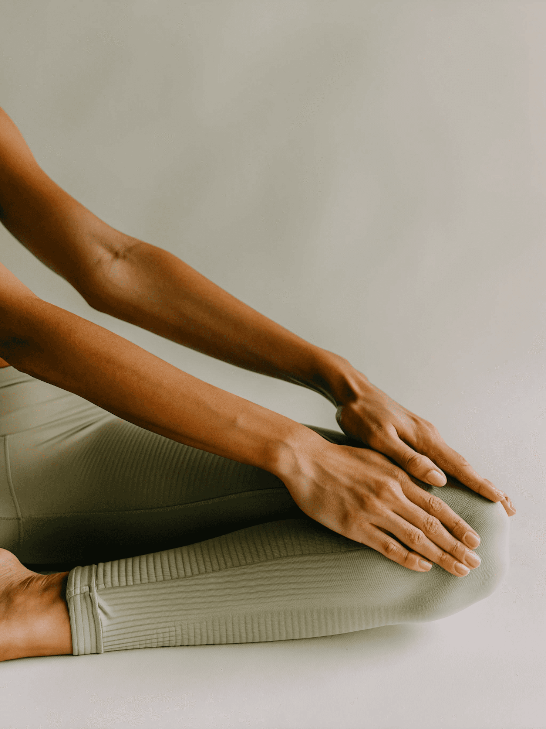 Close-up of hands resting on knees in a calm pose, wearing beige ribbed leggings against a neutral background. Minimalist and serene vibe.