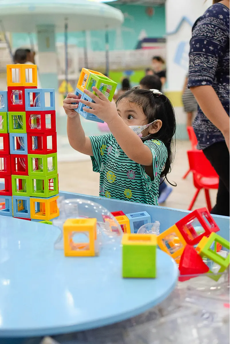A young girl stacking colorful building blocks at a classroom activity table