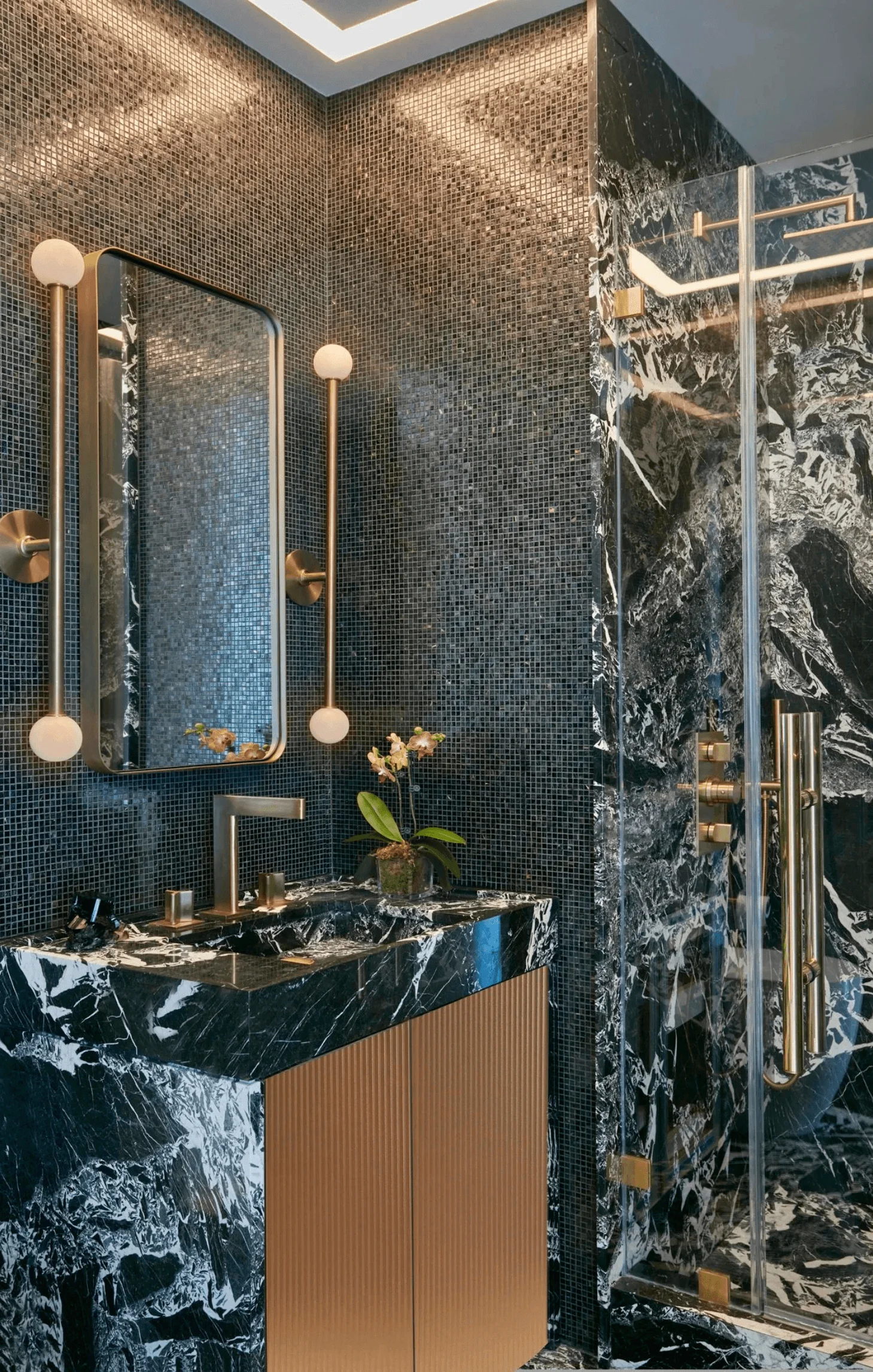 A bathroom vanity in black and white marble with brass fixtures, set against a mosaic tile wall