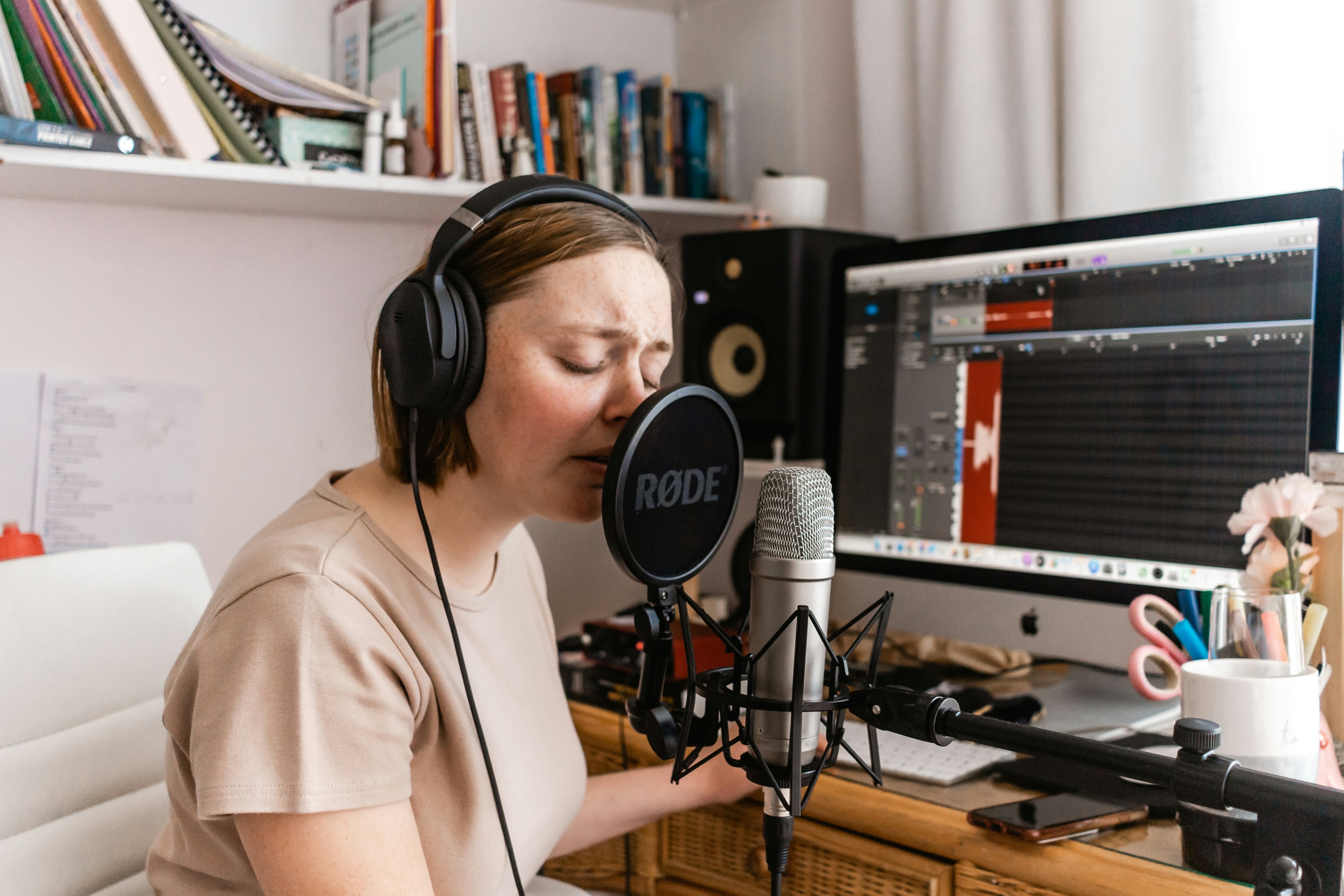 Woman singing into studio mic with a home music production setup background