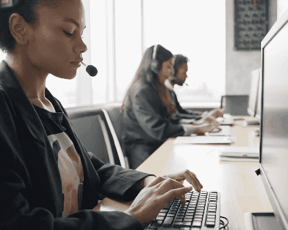 Photo of three women sitting at a table with headsets, typing on their computers, focused on their work, indicating a customer service department.