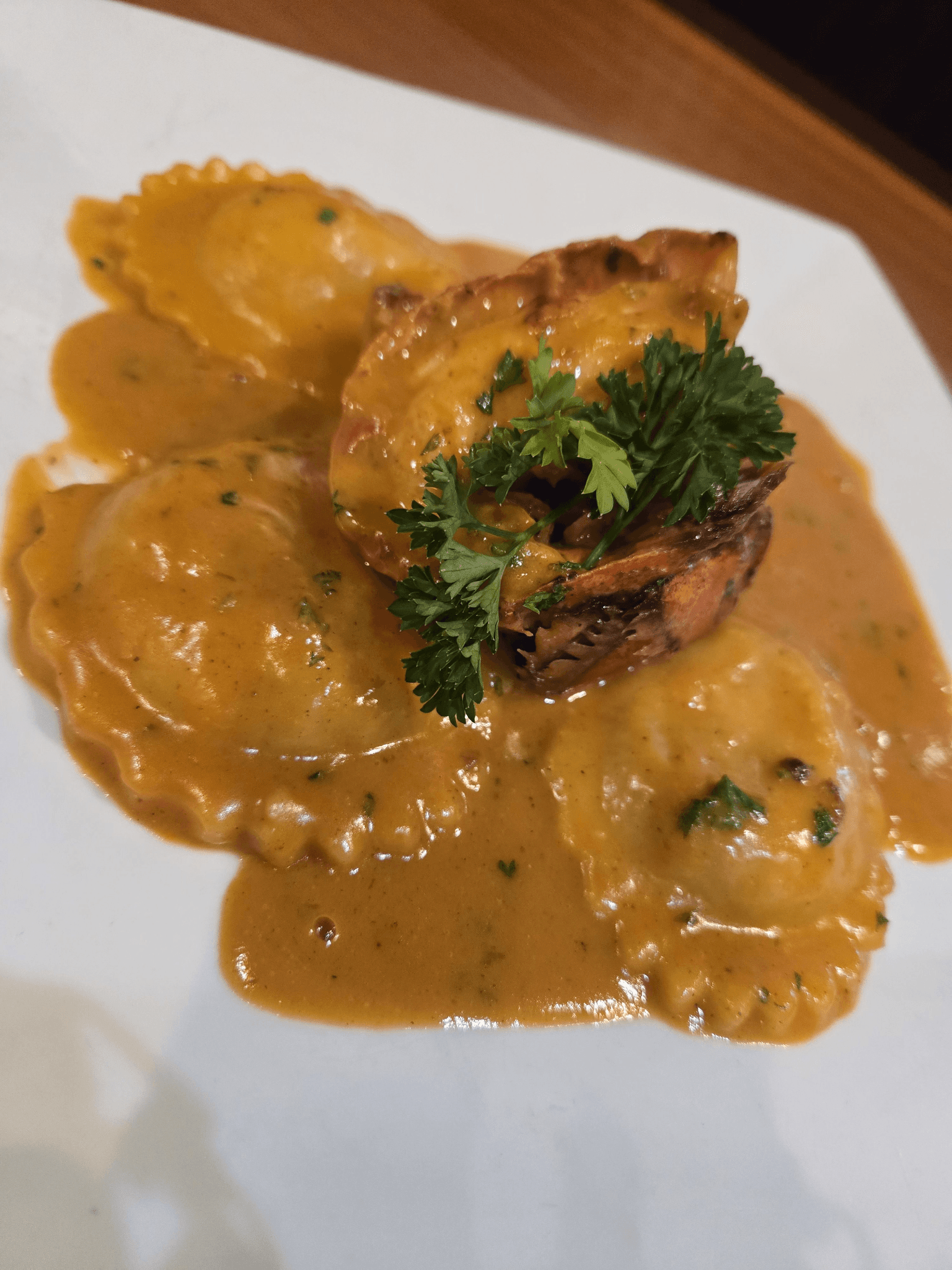 Lobster ravioli topped with grilled lobster in a creamy orange sauce, garnished with fresh parsley.