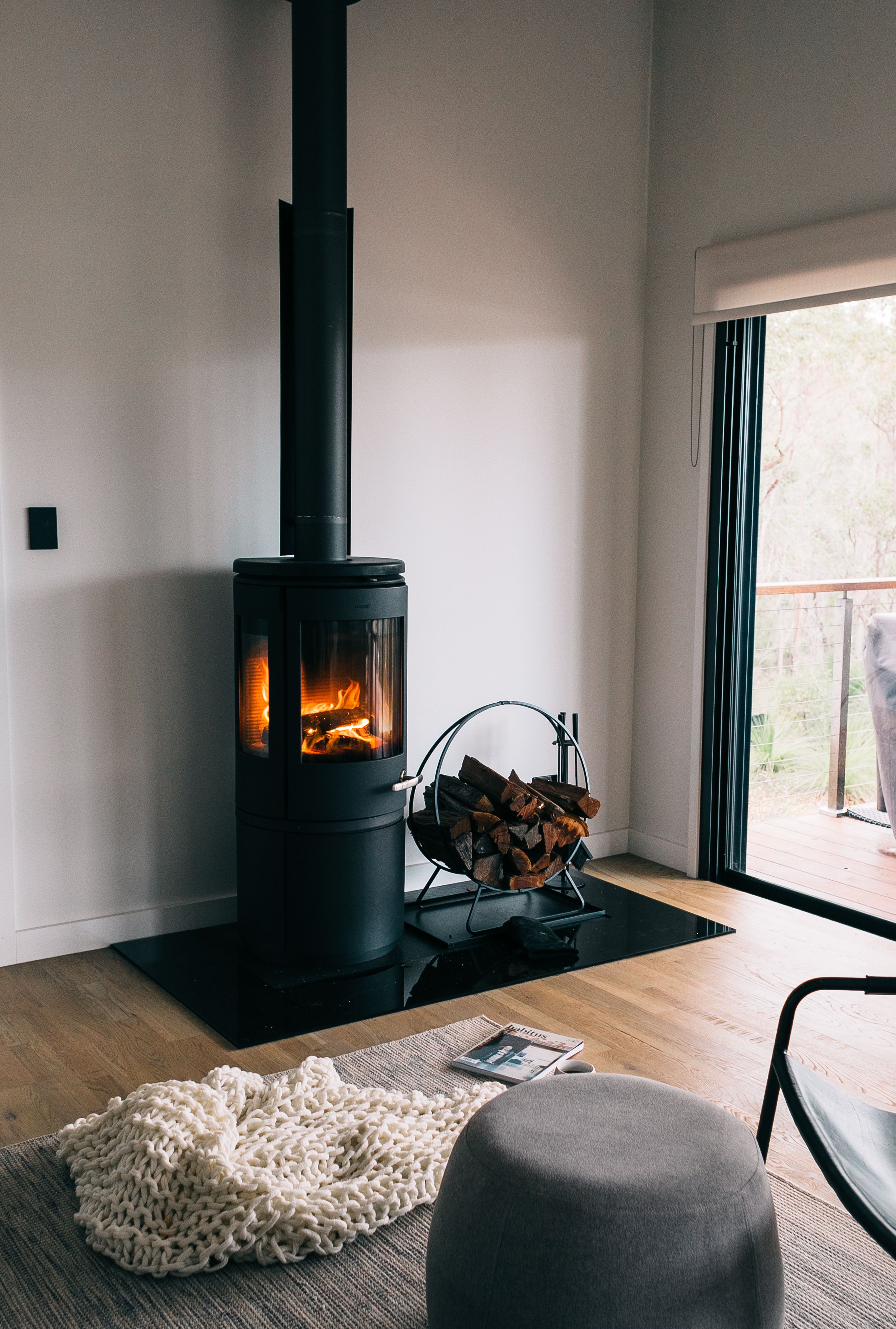 A modern living room centered around a wood-burning stove, with comfortable seating, soft neutral colors, and a warm, relaxing atmosphere.