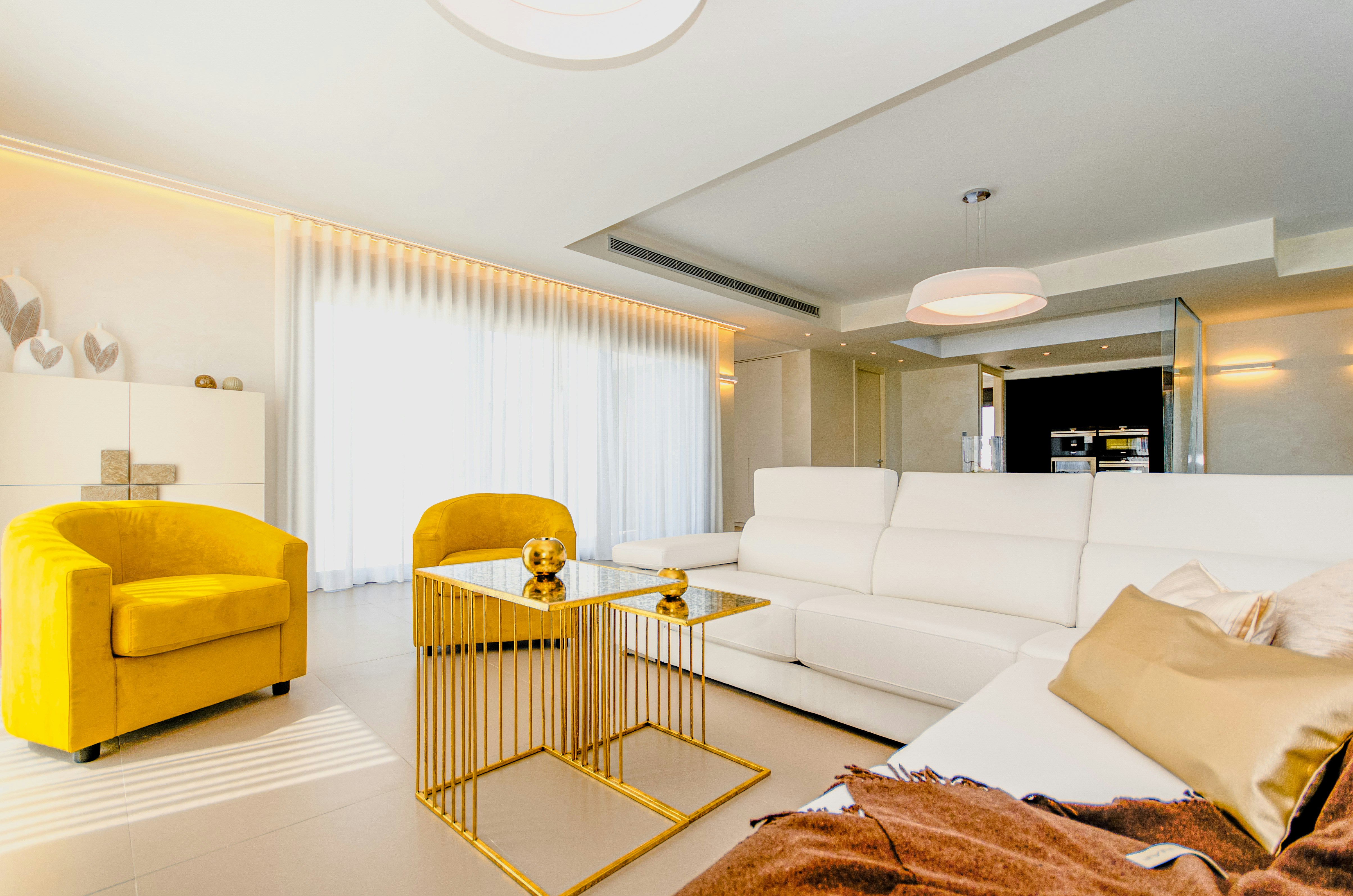 A minimal swiss interior with 2 yellow arm chairs, a white sofa and gols cofee table