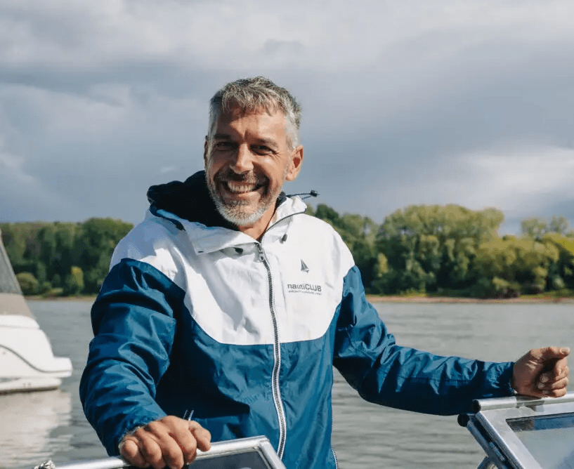 Skipper Stefano in nautiCLUB Jacke lachend am Steuerstand eines Motorboots auf dem Fluss