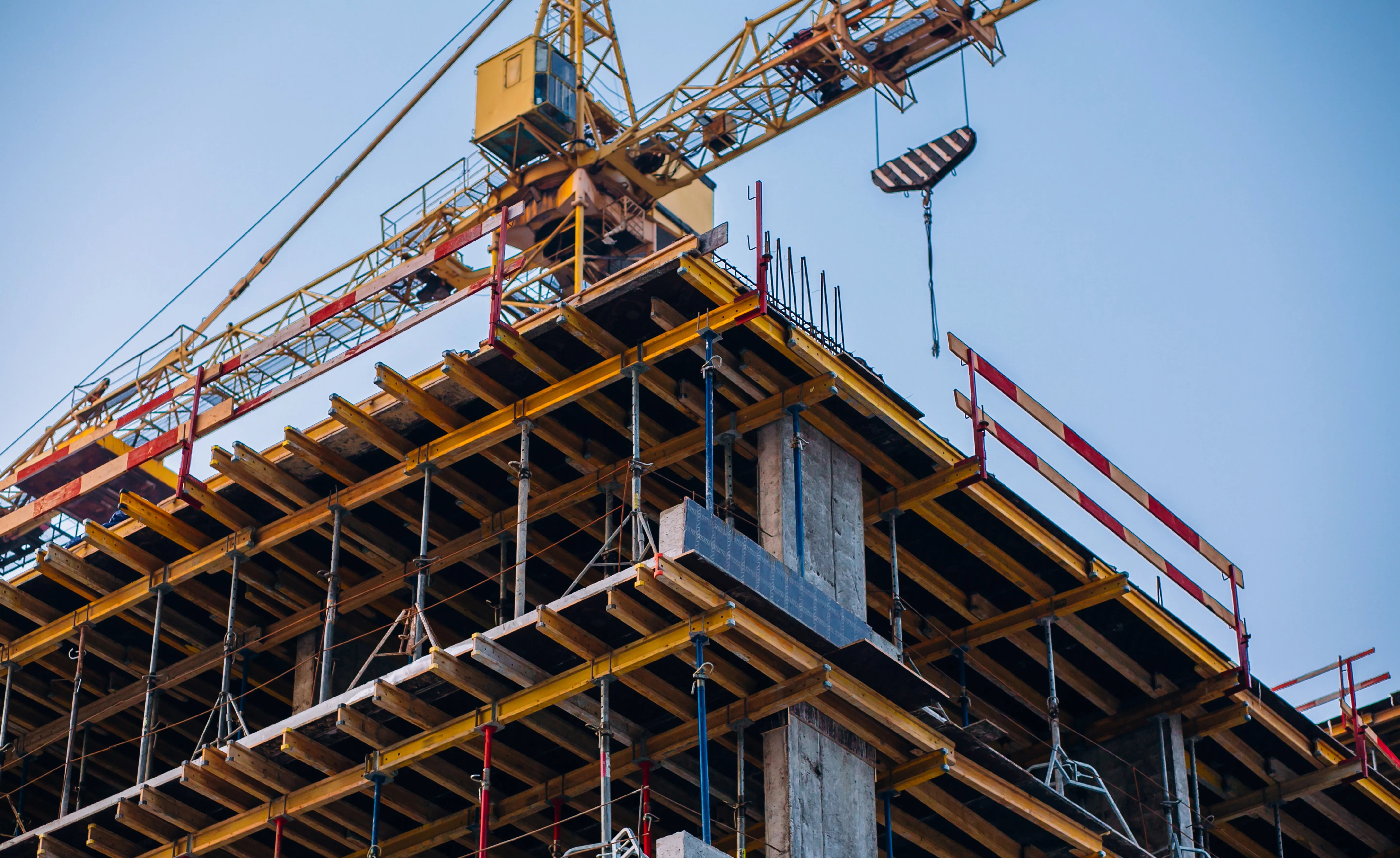 High-rise residential buildings under construction with yellow tower cranes under a clear blue sky.