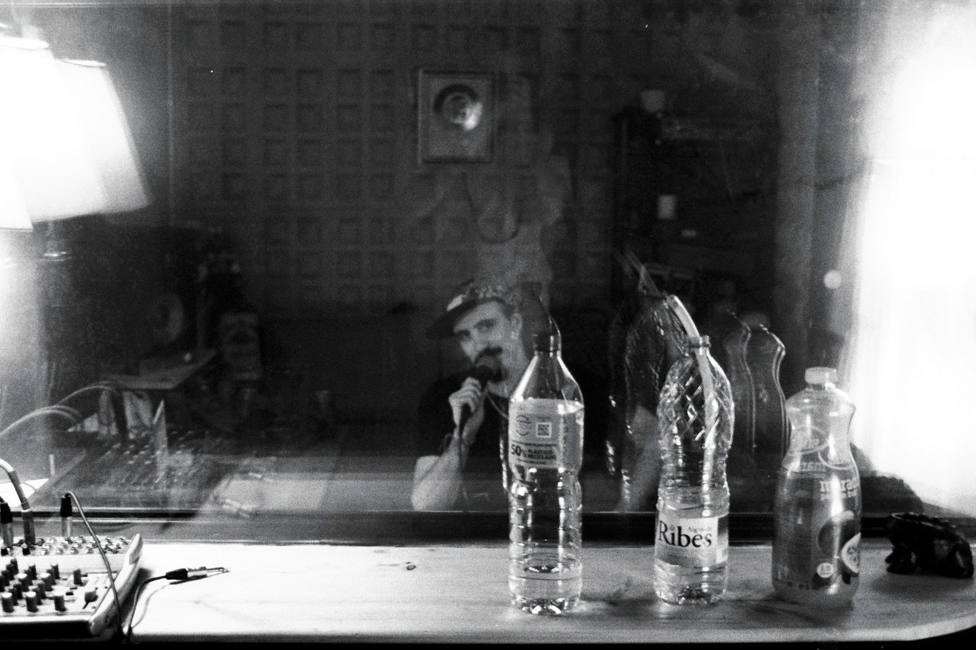 A black and white image of several glass bottles and containers on a table, illuminated by bright lights.