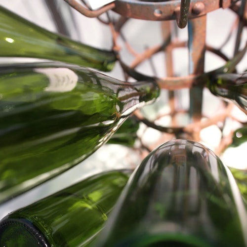 Gröna glasflaskor som förvaras upp och ner i ett metallställ, sedda underifrån.