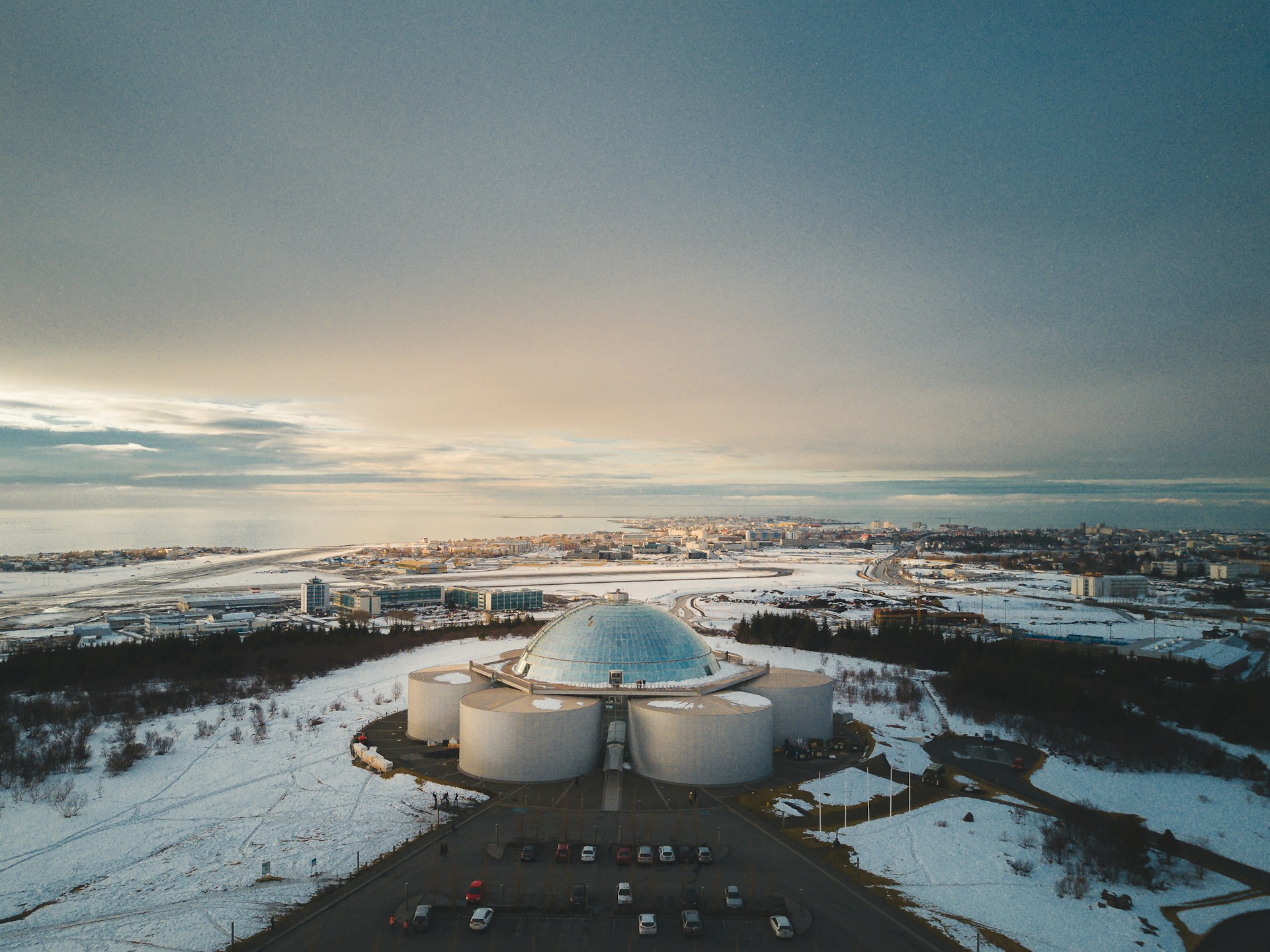 Perlan stands above Reykjavik, Iceland, with winter scenery and coastal views in the distance.