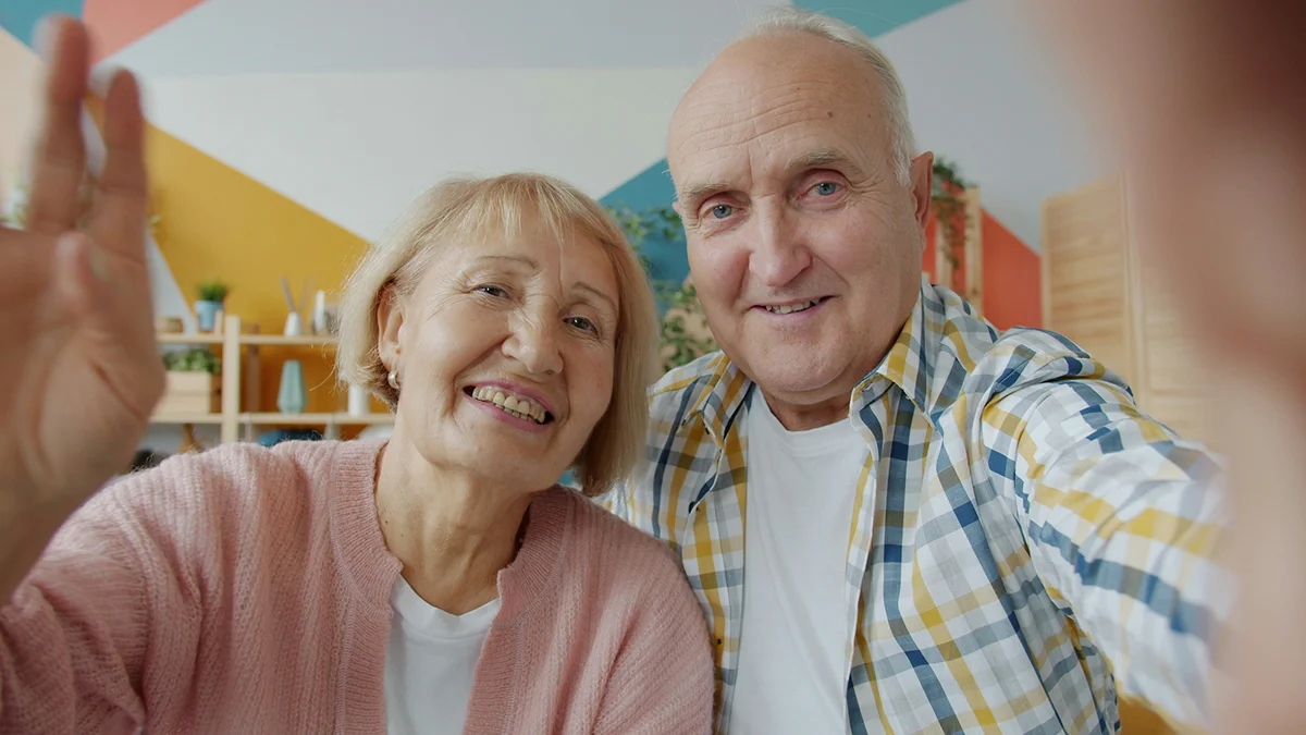An older couple smiling and waving toward the camera.