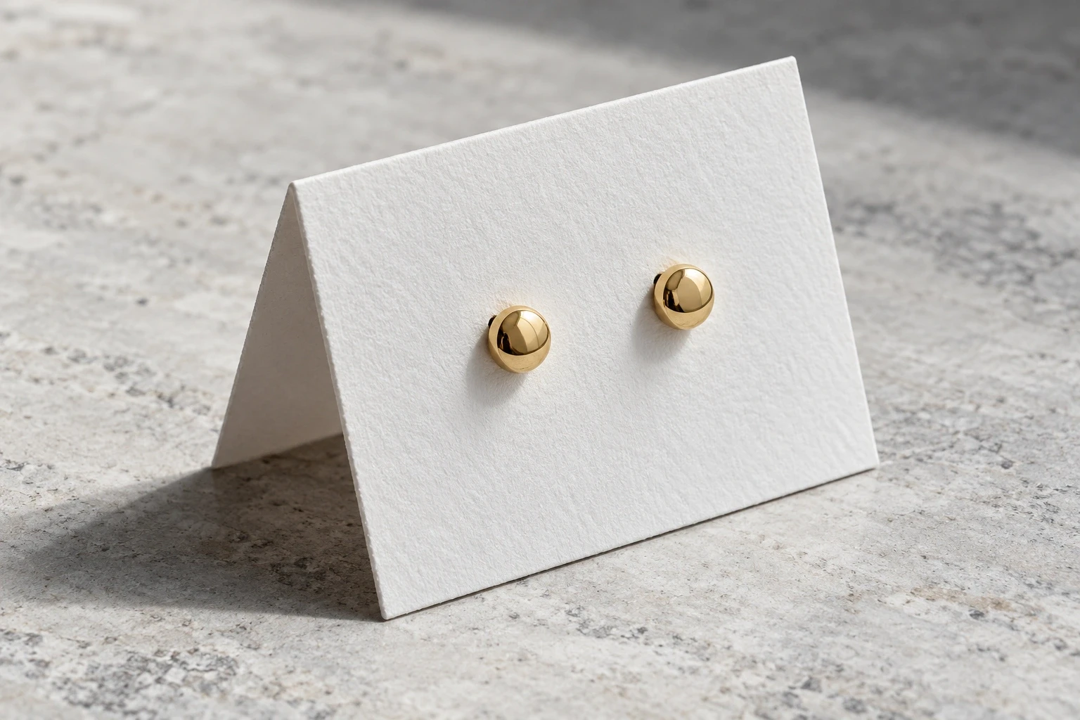 Conceptual pair of round gold stud earrings mounted on unprinted folded white card