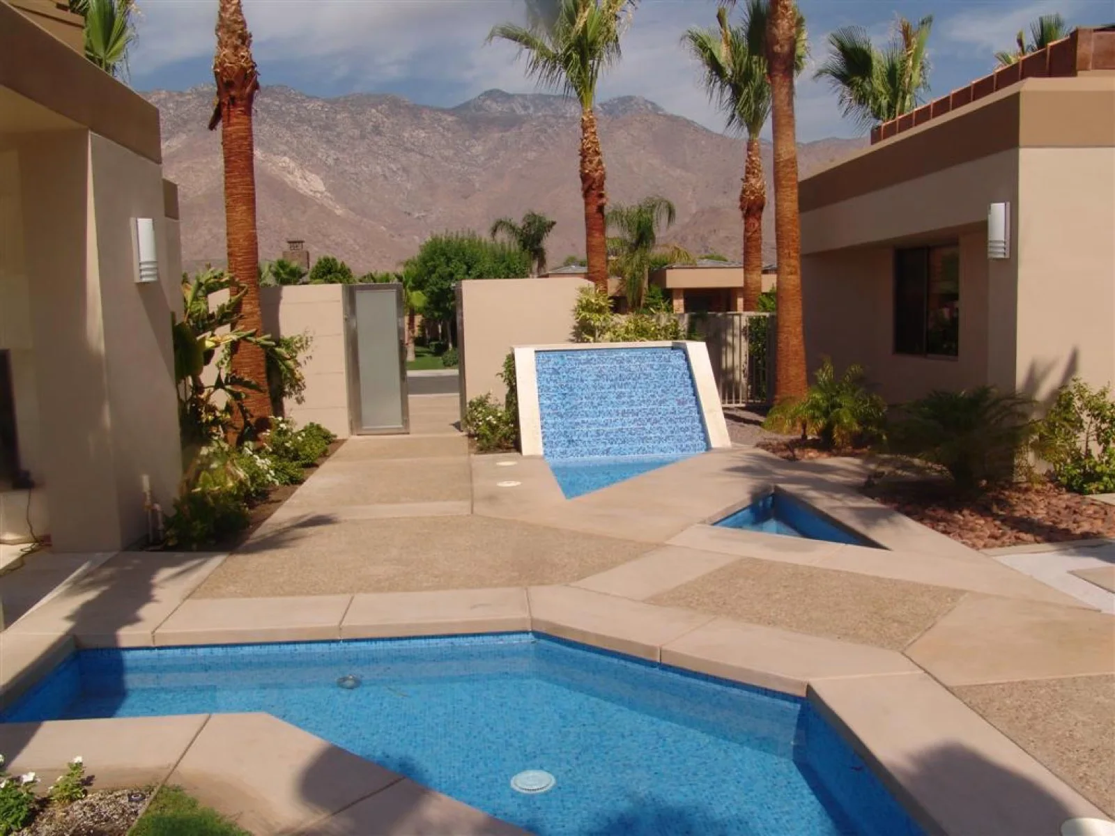 Mosaic-clad water wall spilling into an all-tile glass pool and spa at a Palm Springs residence, mountains beyond