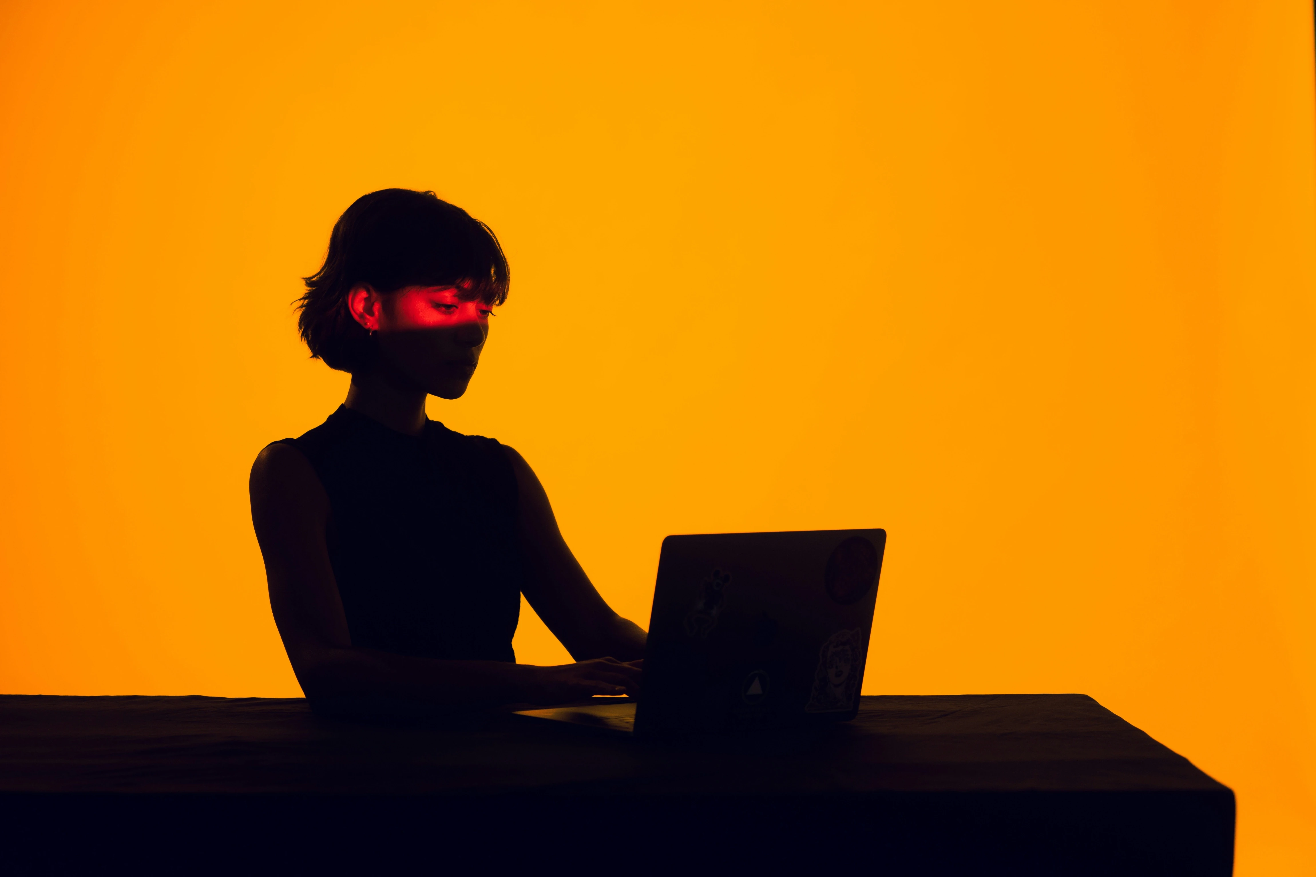 Silhouette einer fokussierten Person, die an einem Laptop arbeitet, vor einem warmen orangefarbenen Hintergrund – Sinnbild für konzentriertes digitales Arbeiten und strategische Gestaltung.