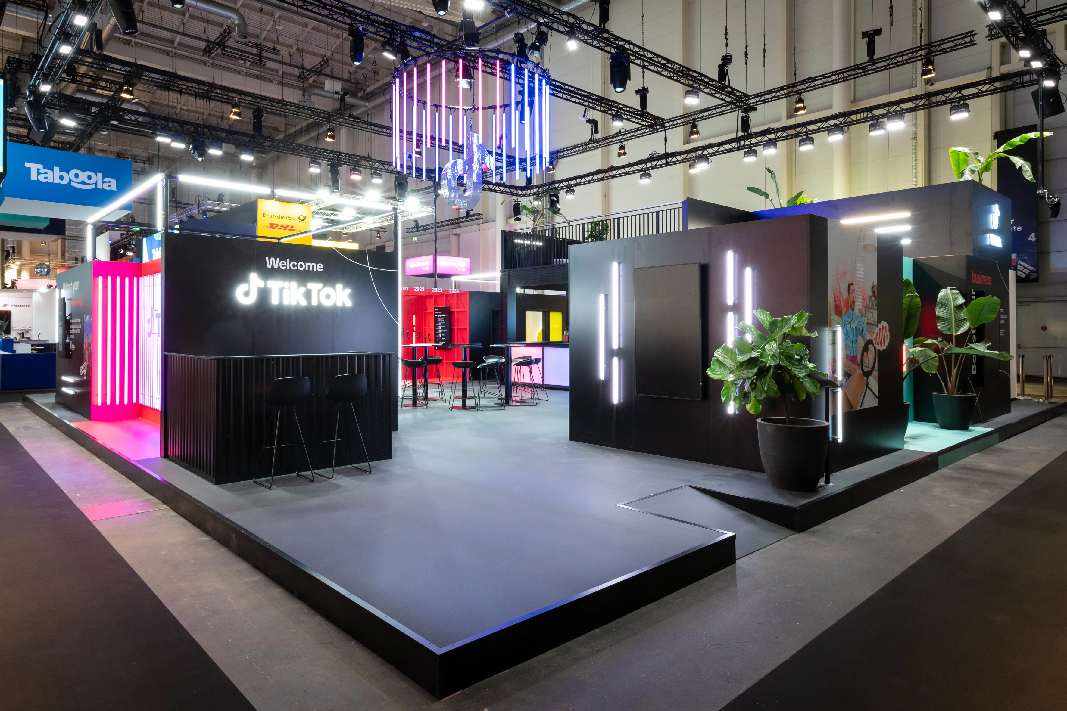 The black TikTok booth at OMR with Welcome counter, neon light tubes and a crown-like light installation above.
