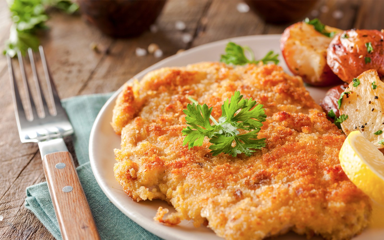 Wiener Schnitzel with roasted potatoes and lemon slice on a plate.