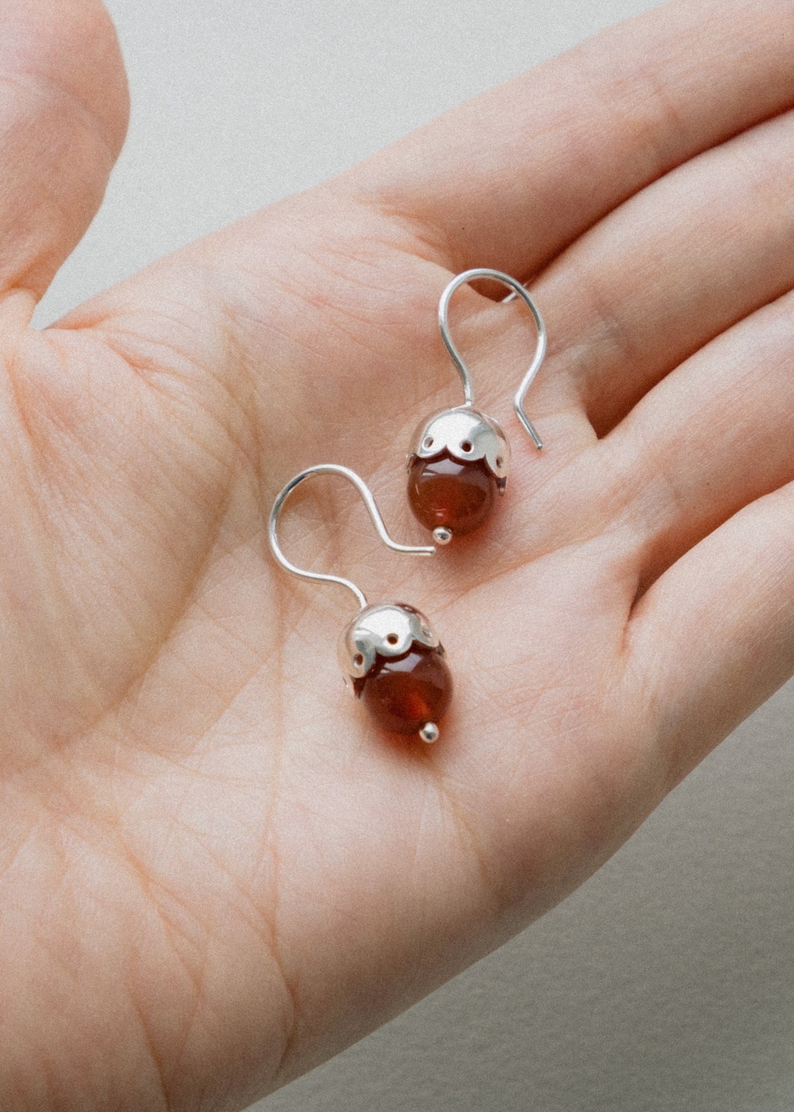 Silver earrings with red carnelian beads held in a hand against a neutral background