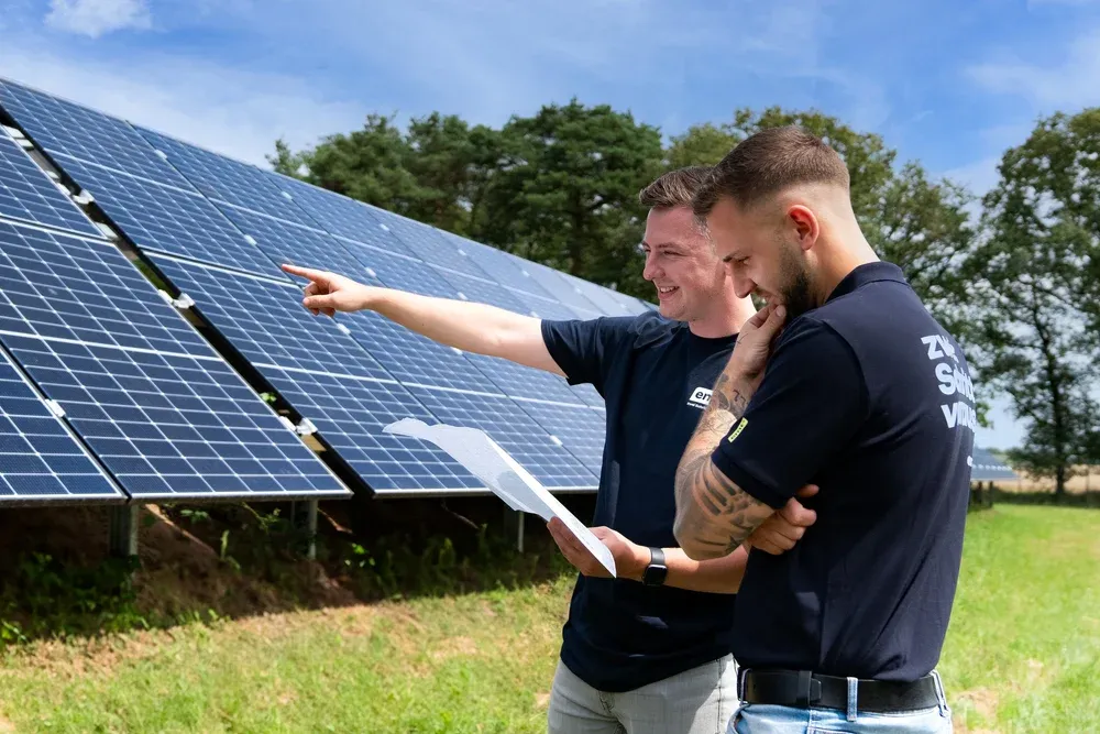 Zwei Männer prüfen Solarmodule im Freien, einer zeigt darauf.