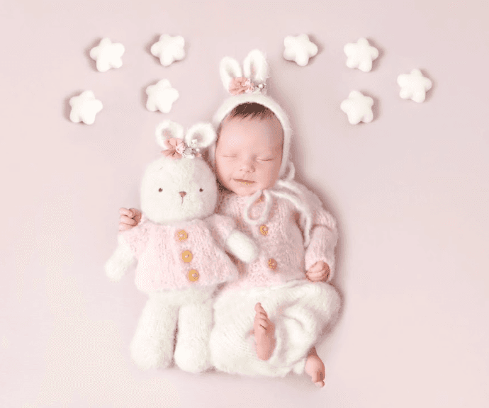 Baby girl with a plush rabbit toy with a seamless stretch pink background.