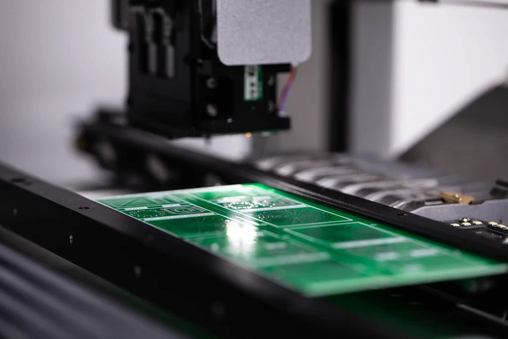 Close-up of a green printed circuit board being manufactured on automated production equipment.