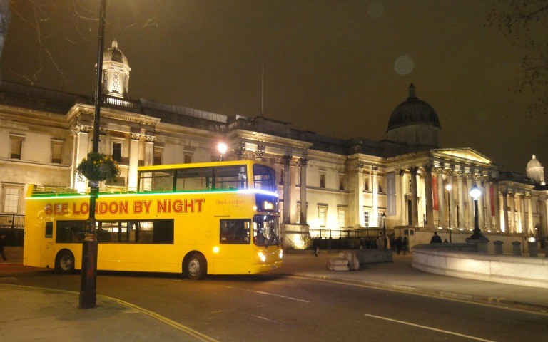 Yellow double-decker bus in front of London's National Gallery at night.
