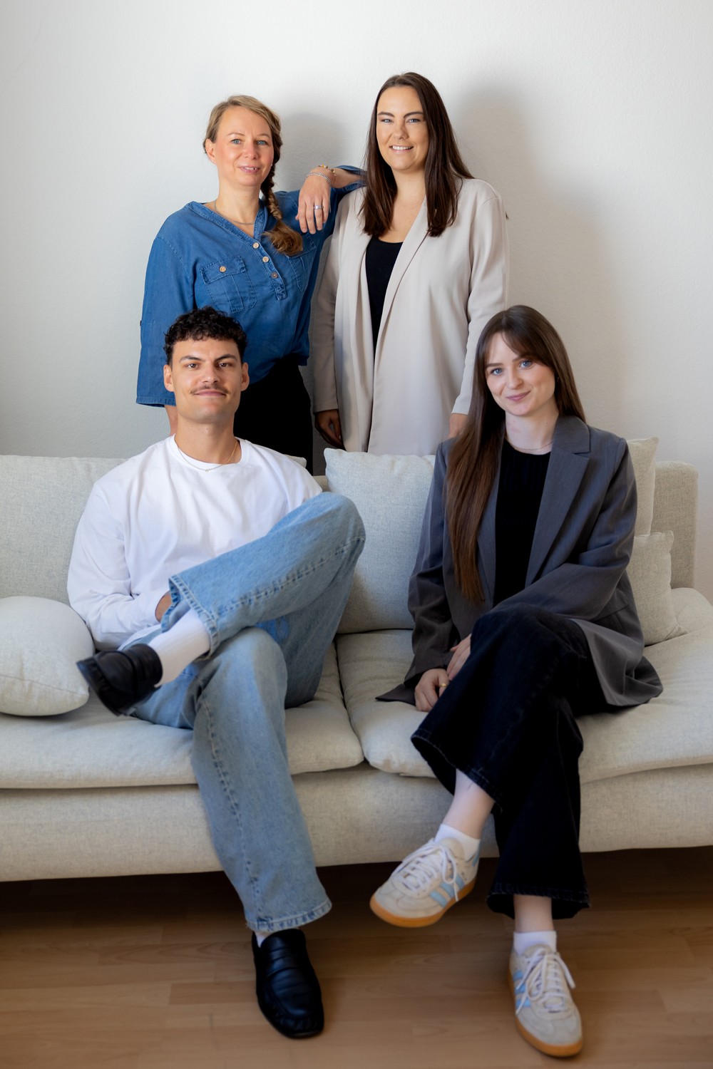 Vier Teammitglieder lächelnd auf und hinter einem hellen Sofa vor weißer Wand.