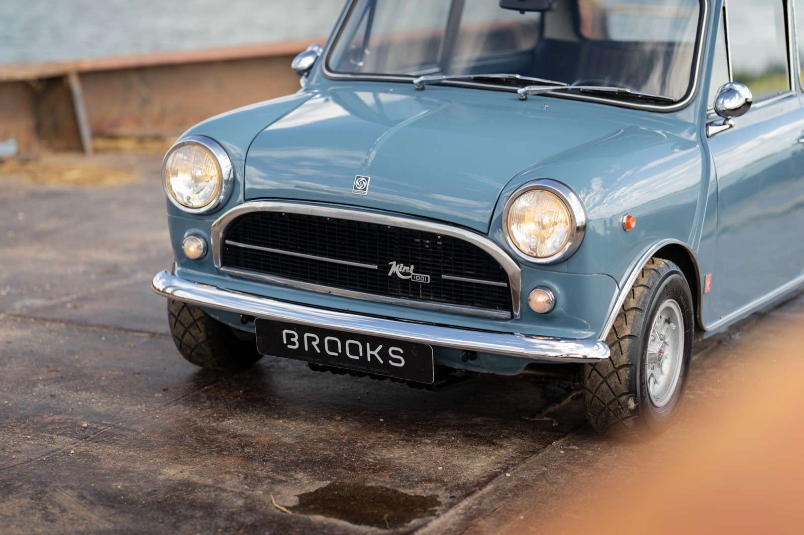 A vintage blue car parked on a wooden platform, showcasing its classic front grille and headlights.