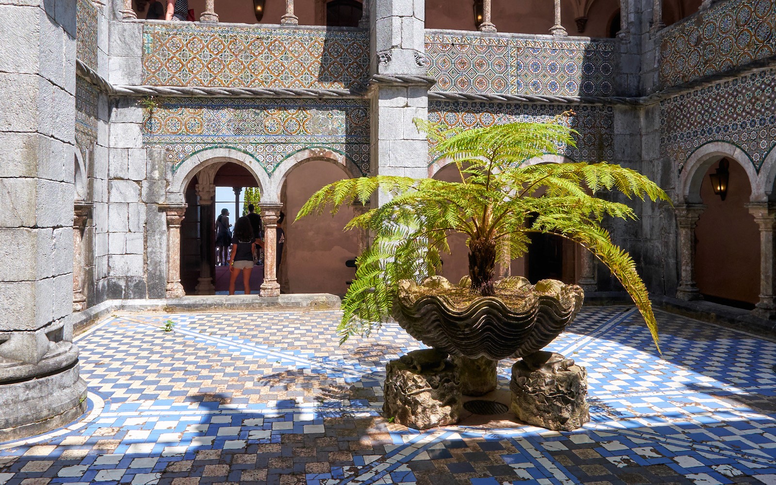 Koridor dengan lengkungan berhias dan pakis pusat dalam bekas berbentuk cangkerang.