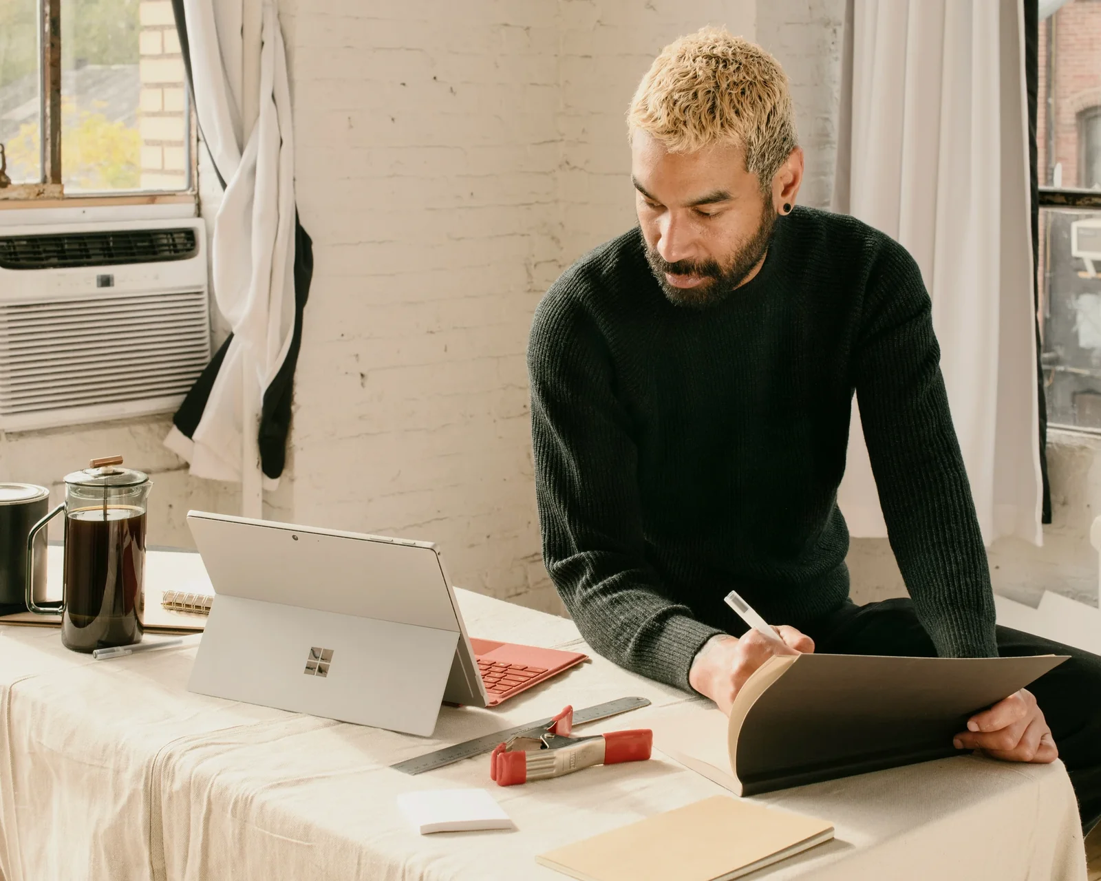 Man in dark sweater working at desk with laptop and tablet in modern office space.