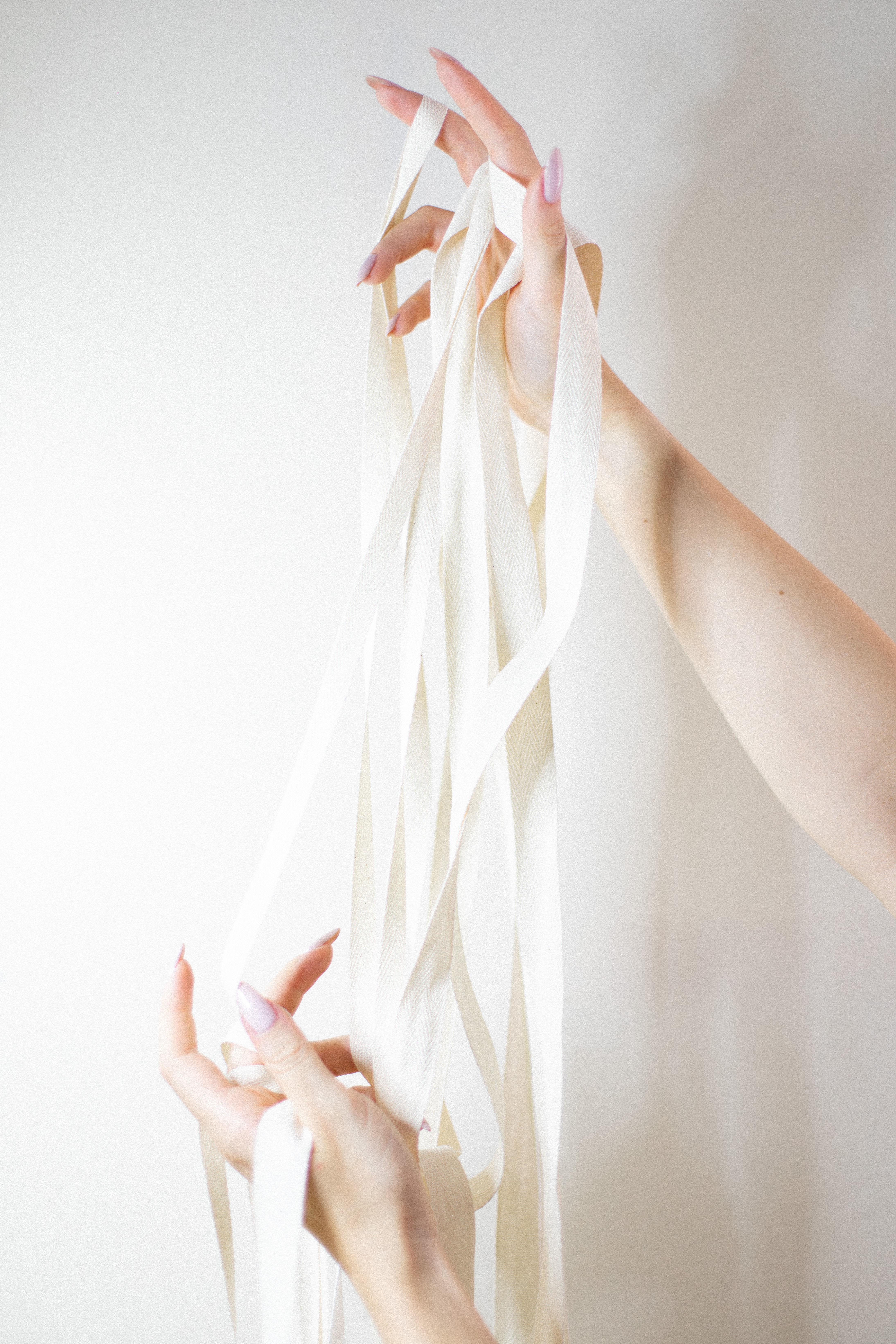 Two hands holding a cascade of long cream ribbons against a plain light background.