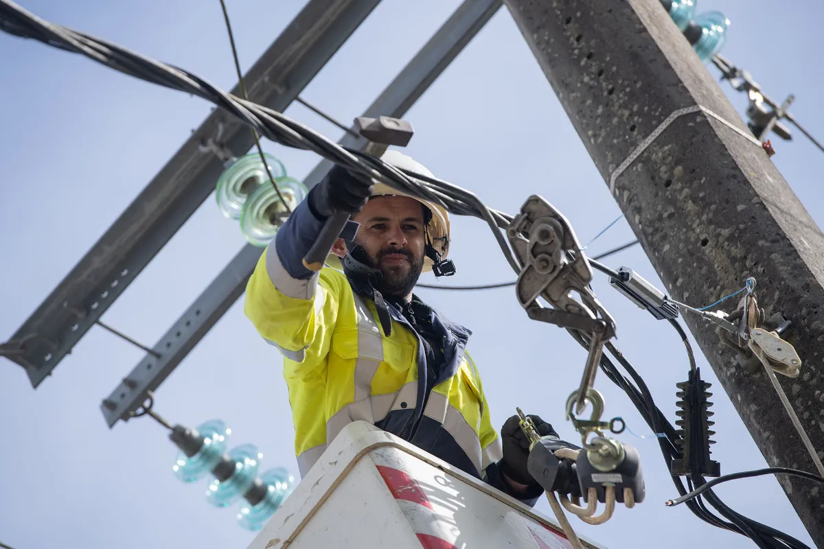 Électricien en gilet haute visibilité travaillant sur des lignes électriques aériennes depuis une nacelle élévatrice