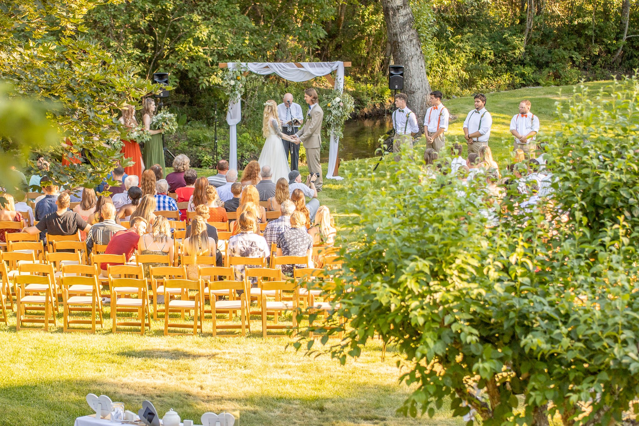 A wedding ceremony from a distance, brown chairs, green trees