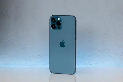 白い表面に立っている青いiPhone、トリプルカメラシステム付き