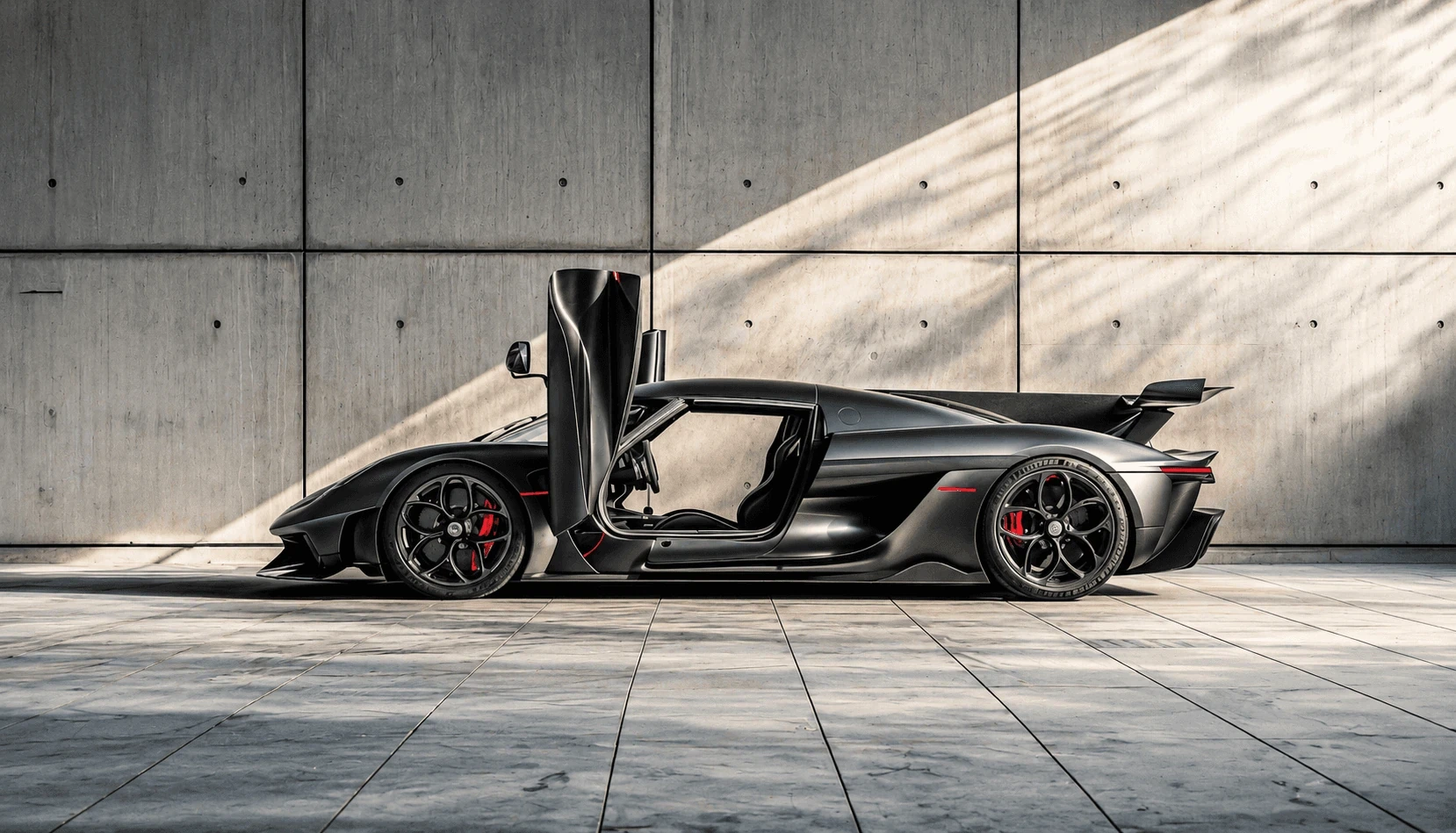 Sleek, dark gray sports car with open doors, red brake calipers, parked indoors, bathed in sunlight.