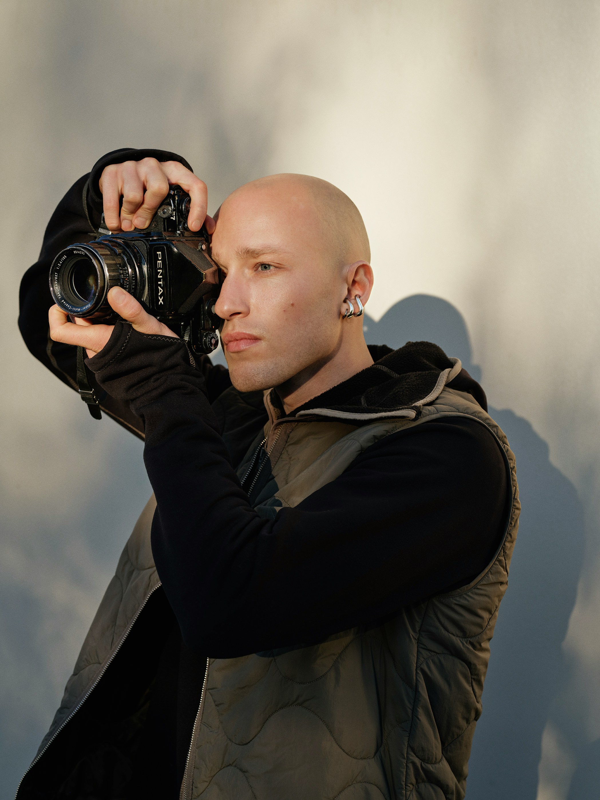 Bald man holding a vintage camera and taking a picture.